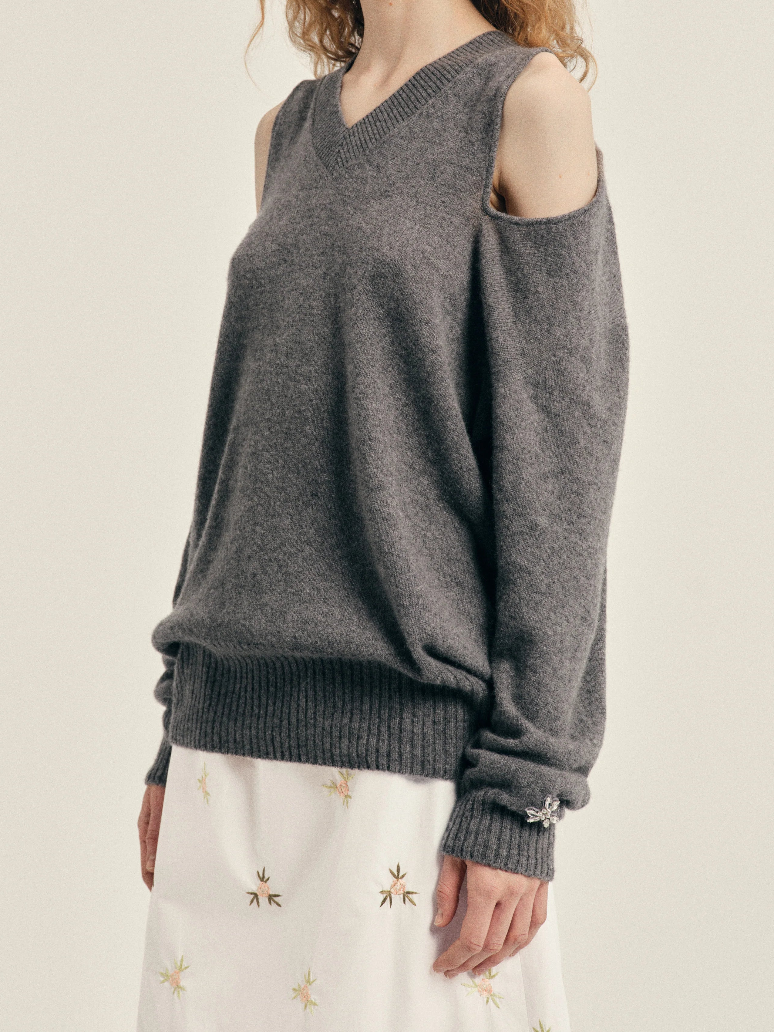 Simone Rocha Relaxed Cashmere Slash V-Neck Jumper With Embellishment in Grey, worn side view showing the V-neckline, open shoulder detail and embellished cuff.