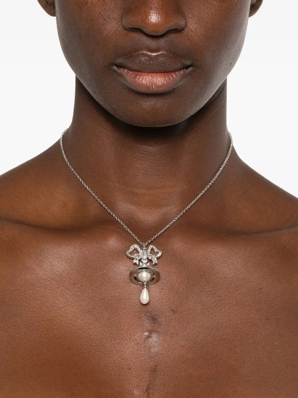 Model wearing Rigoberta Pearl Pendant in Platinum/Crystal Velvet/Creamrose by Vivienne Westwood, fine silver-tone chain with crystal-embellished bow pendant, Orb motif and teardrop pearl drop at neckline, Spring/Summer 2026