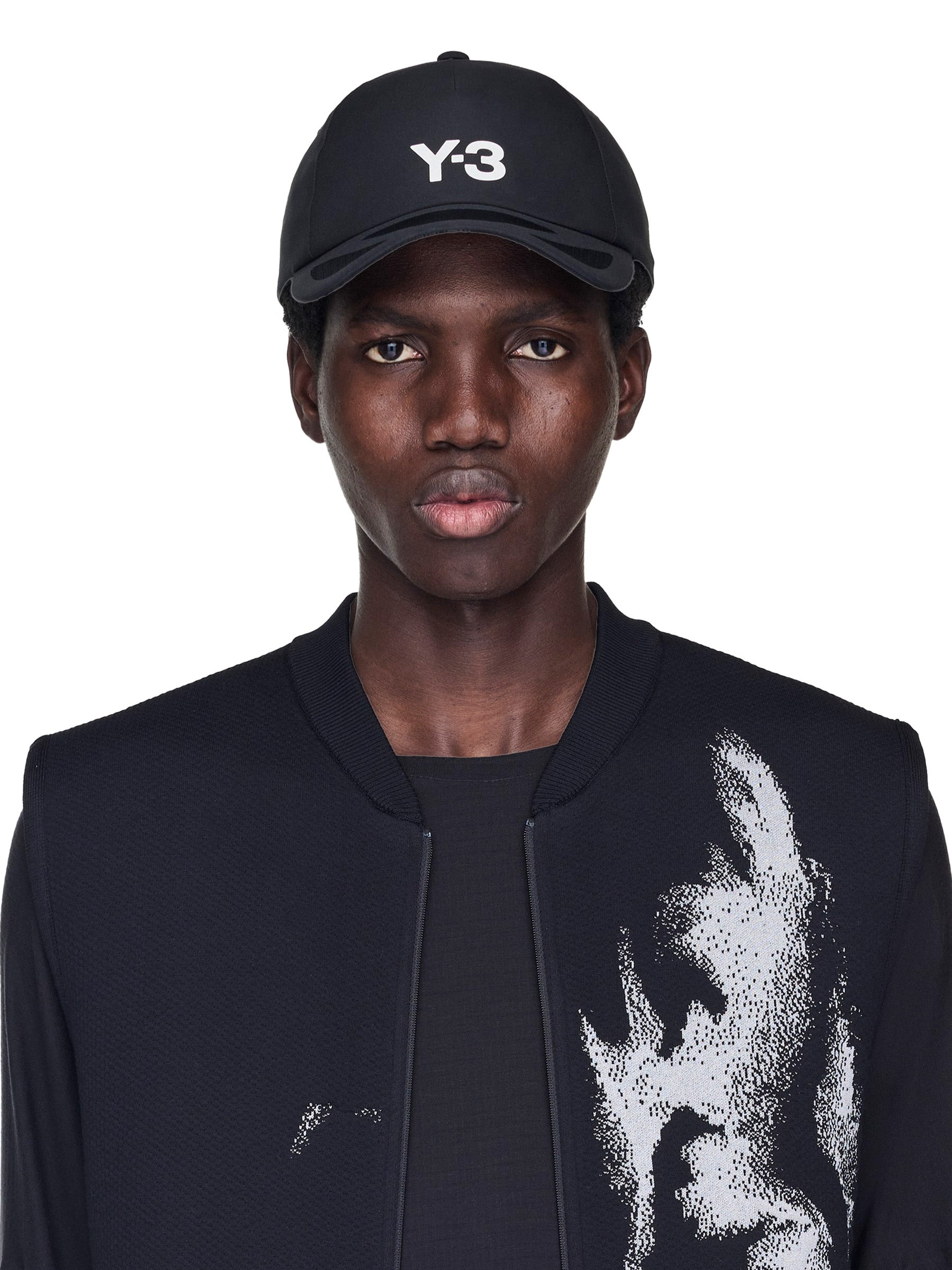 Person wearing a black Y-3 cap and black jacket with white design on a white background