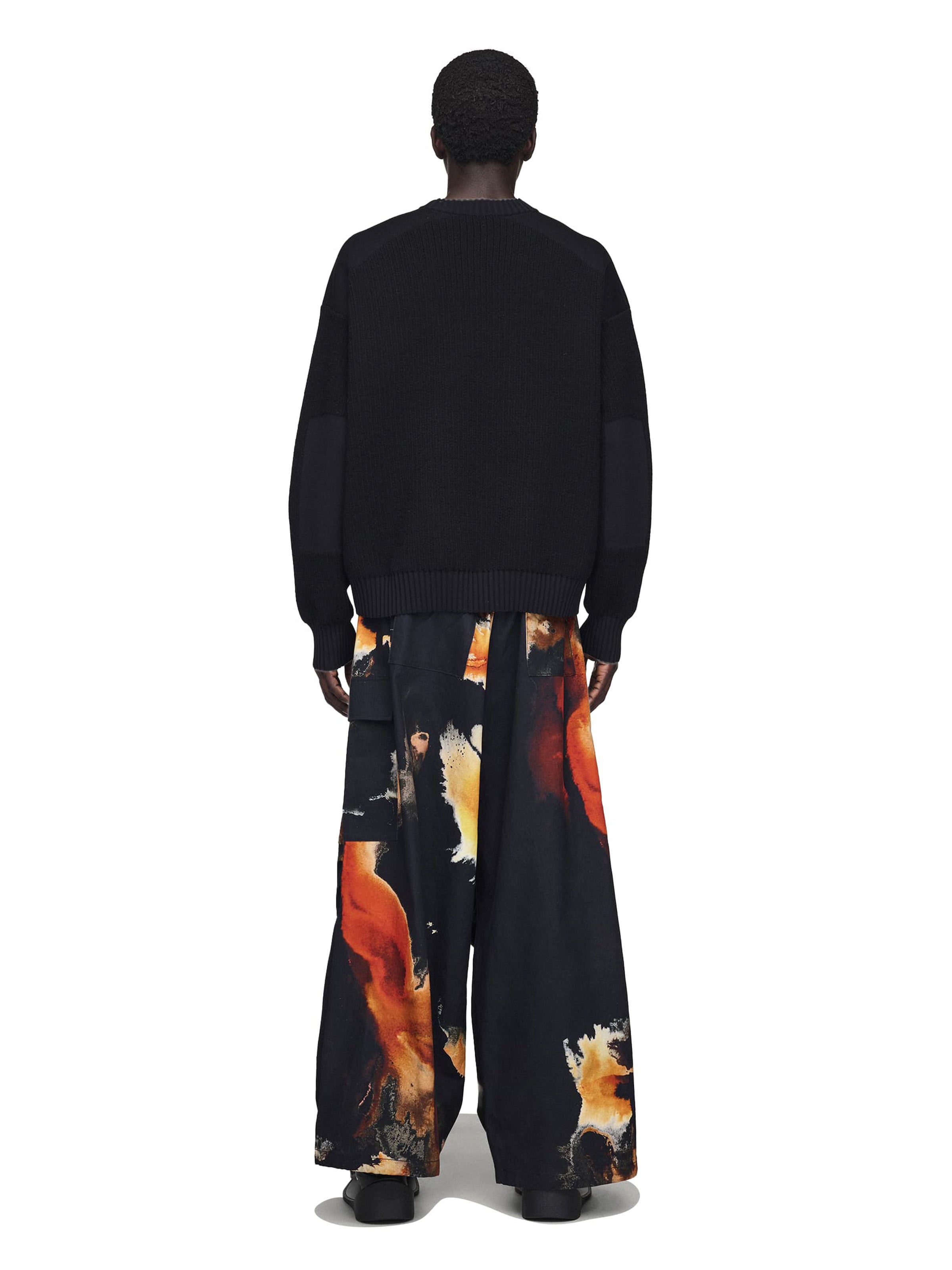 Person wearing a black sweatshirt and colorful pants on a white background
