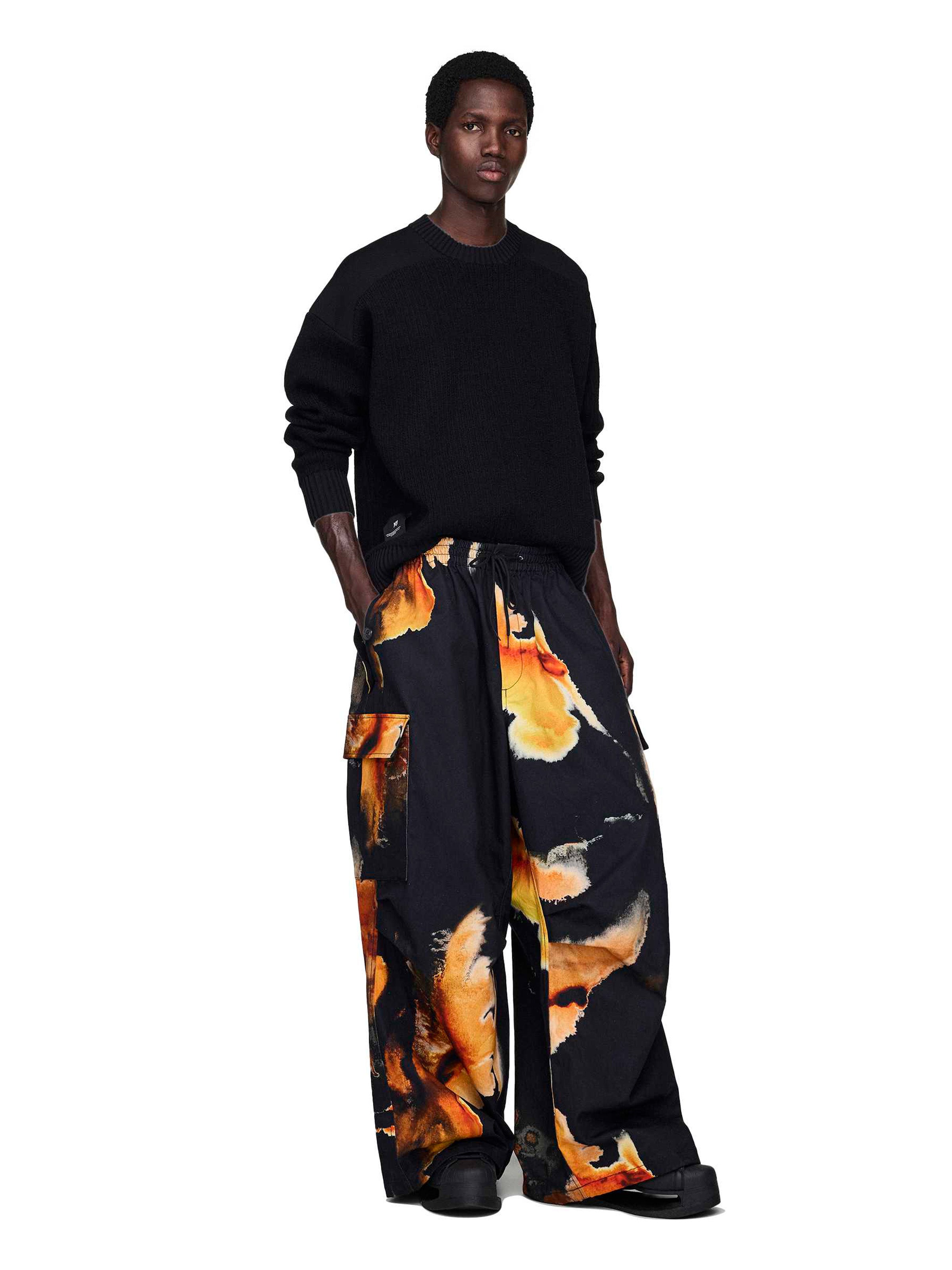 Person wearing a black sweater and wide-leg pants with a colorful abstract pattern on a white background