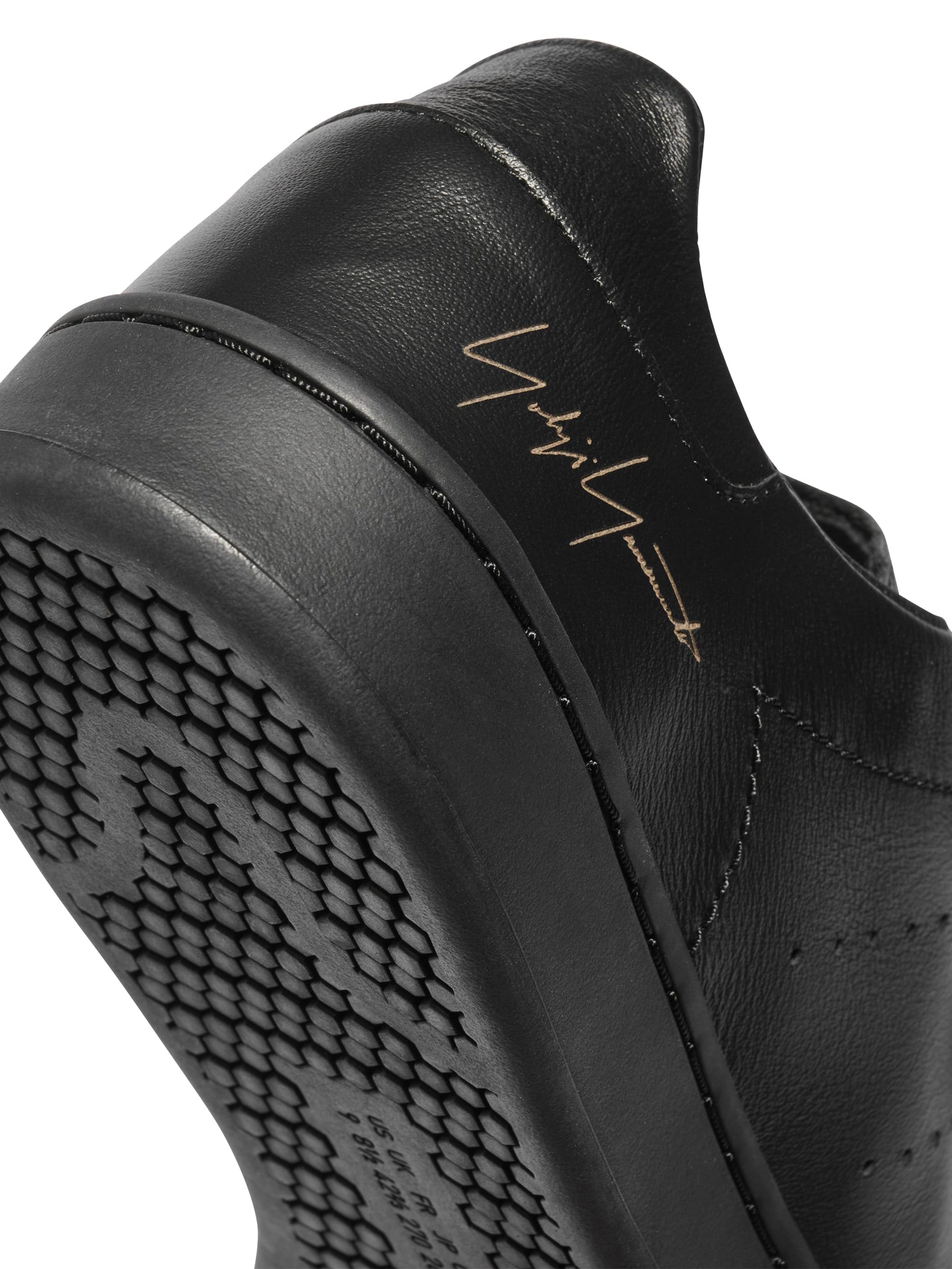 Diagonal close-up of the heel of the Y-3 Stan Smith Hook-and-Loop Shoes in Black, showing the leather upper, heel curve, and subtle signature detail.
