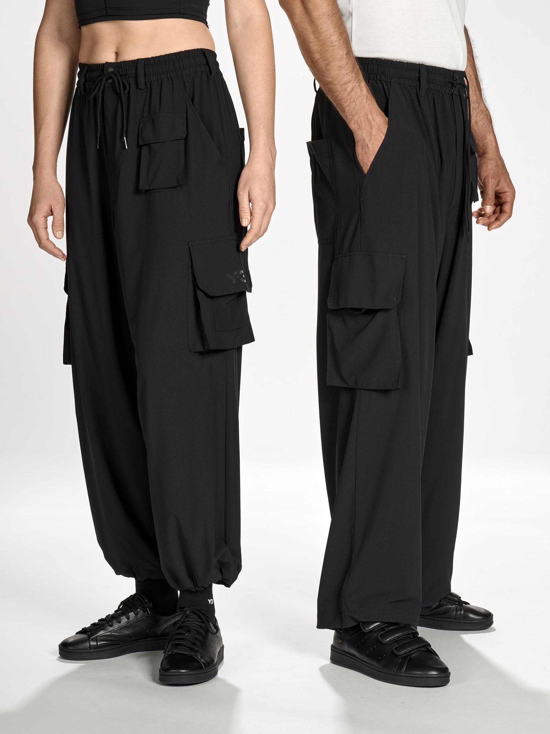 Front view of female and male models wearing Y-3 Utility Straight Tracksuit Pants in Black, showing the loose, straight-leg silhouette and relaxed fit on both.