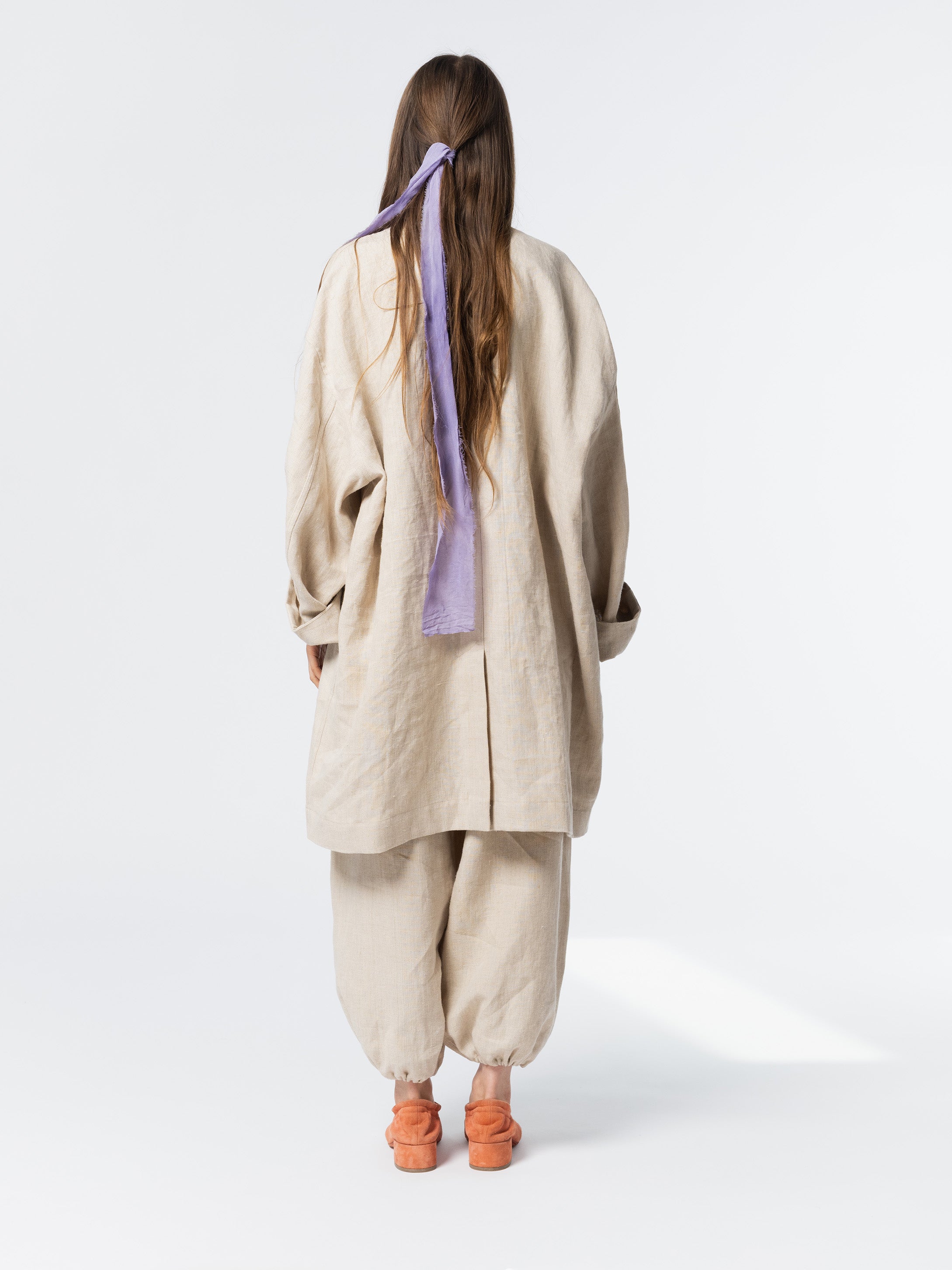 Back view of model wearing the Anntian Trench Jacket Hemp in Natural, an off-white loose-fit hemp jacket, one size