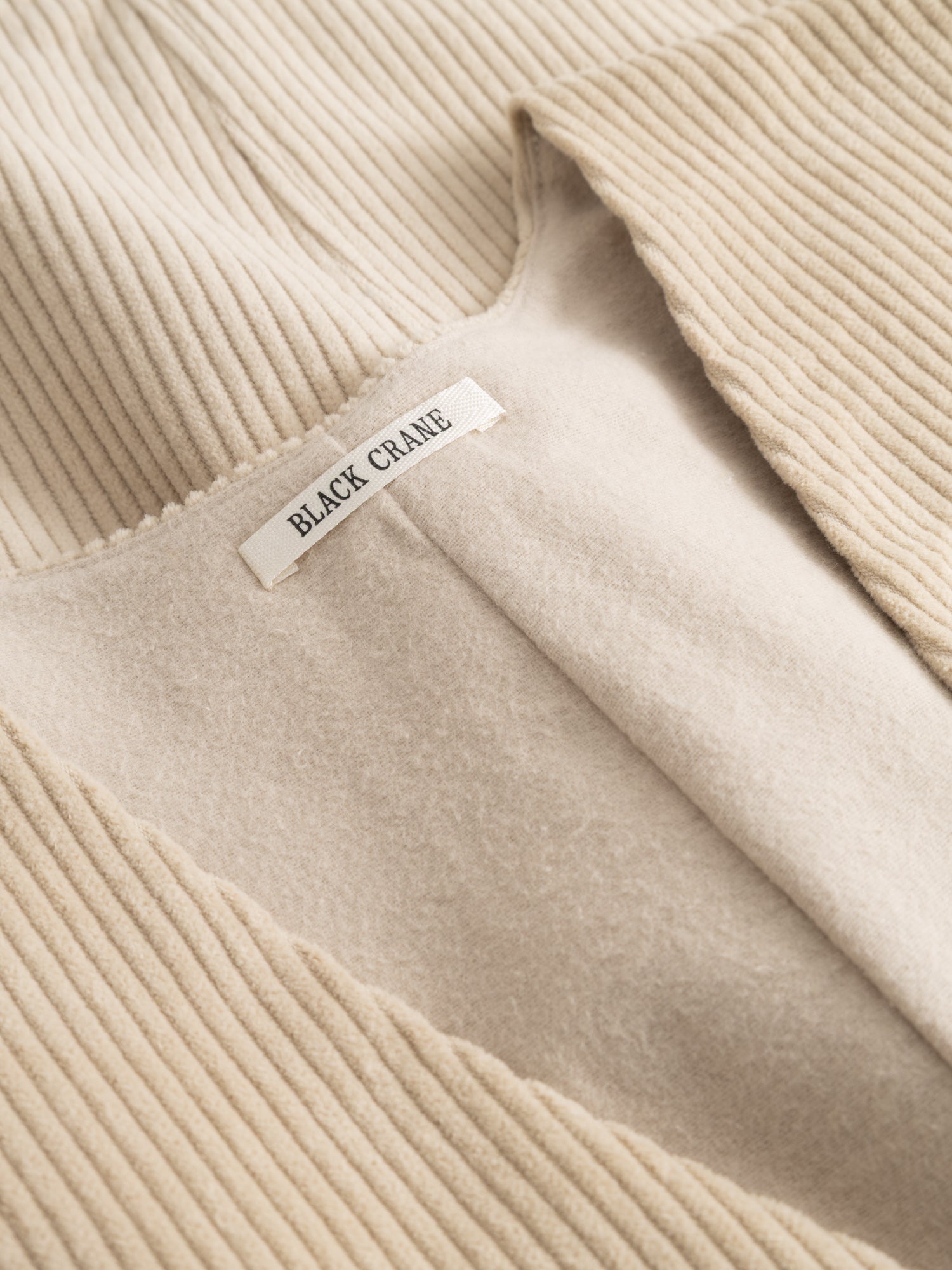 Close-up of the Black Crane Corduroy Vest showing the off-white corduroy texture and the brand label at the neckline.