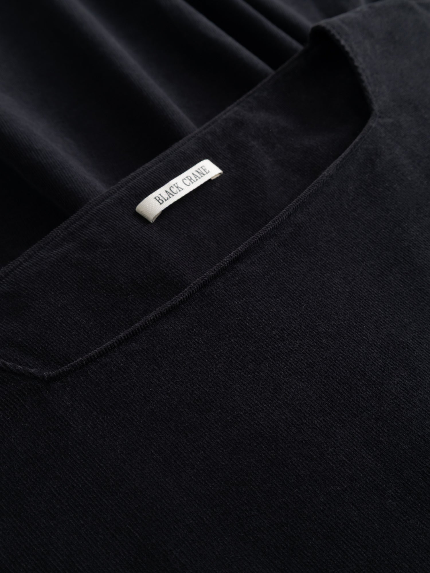 Close-up of the Black Crane Tradi Dress showing the dark navy corduroy texture and the brand label at the neckline.