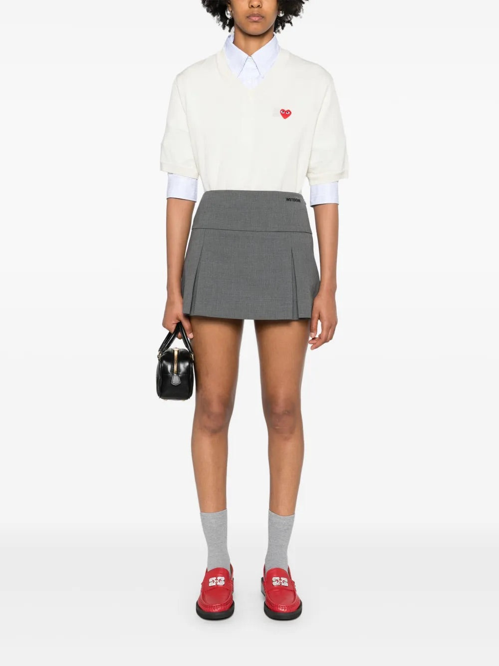 Full-body front view of a female model wearing the Comme des Garçons Play Unisex V-Neck Sweater Short-Sleeve in off white, highlighting the relaxed V-neck silhouette and refined wool construction.
