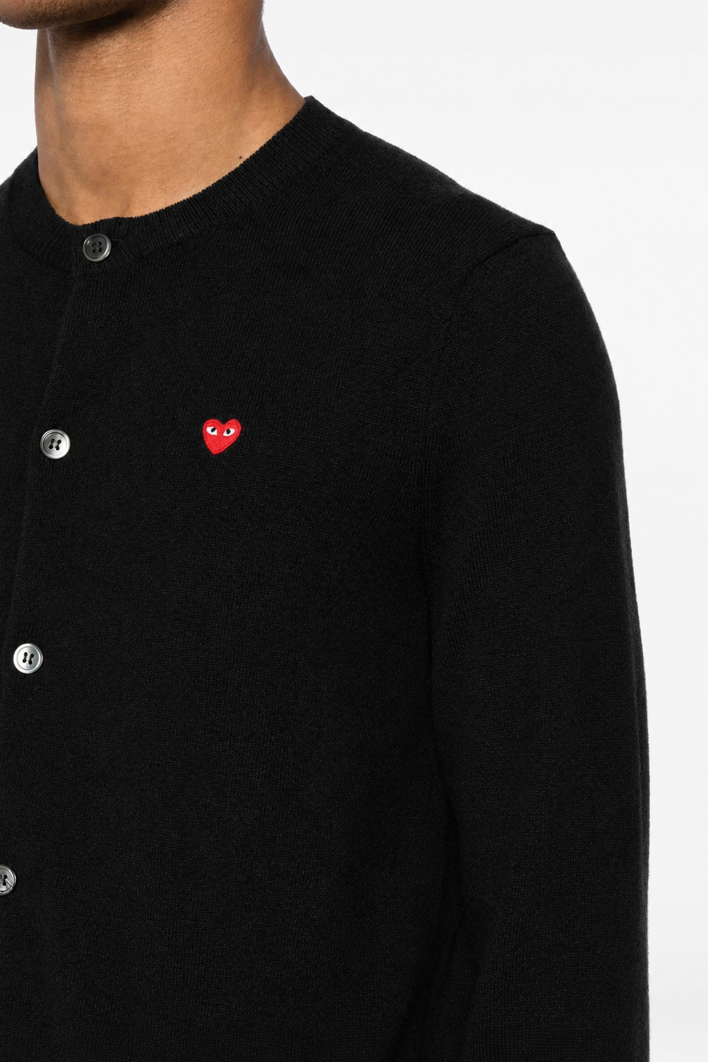 Close-up of Comme des Garçons Play black cardigan showing red embroidered heart logo, round neckline and button closure