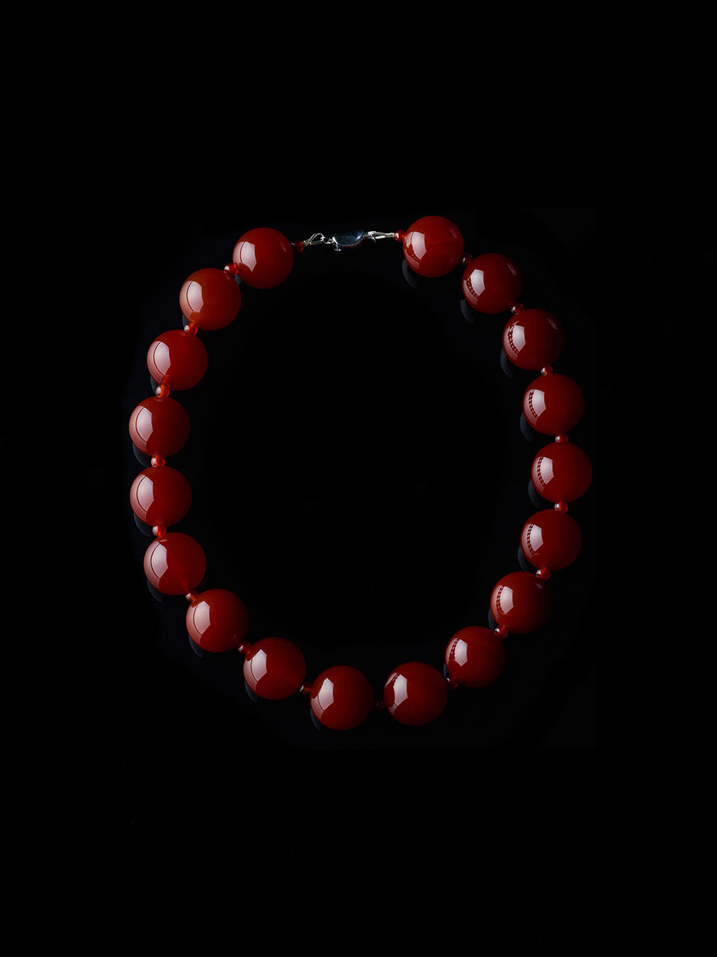 Round and red carnelian necklace with silver clasp from De Silang on a black background