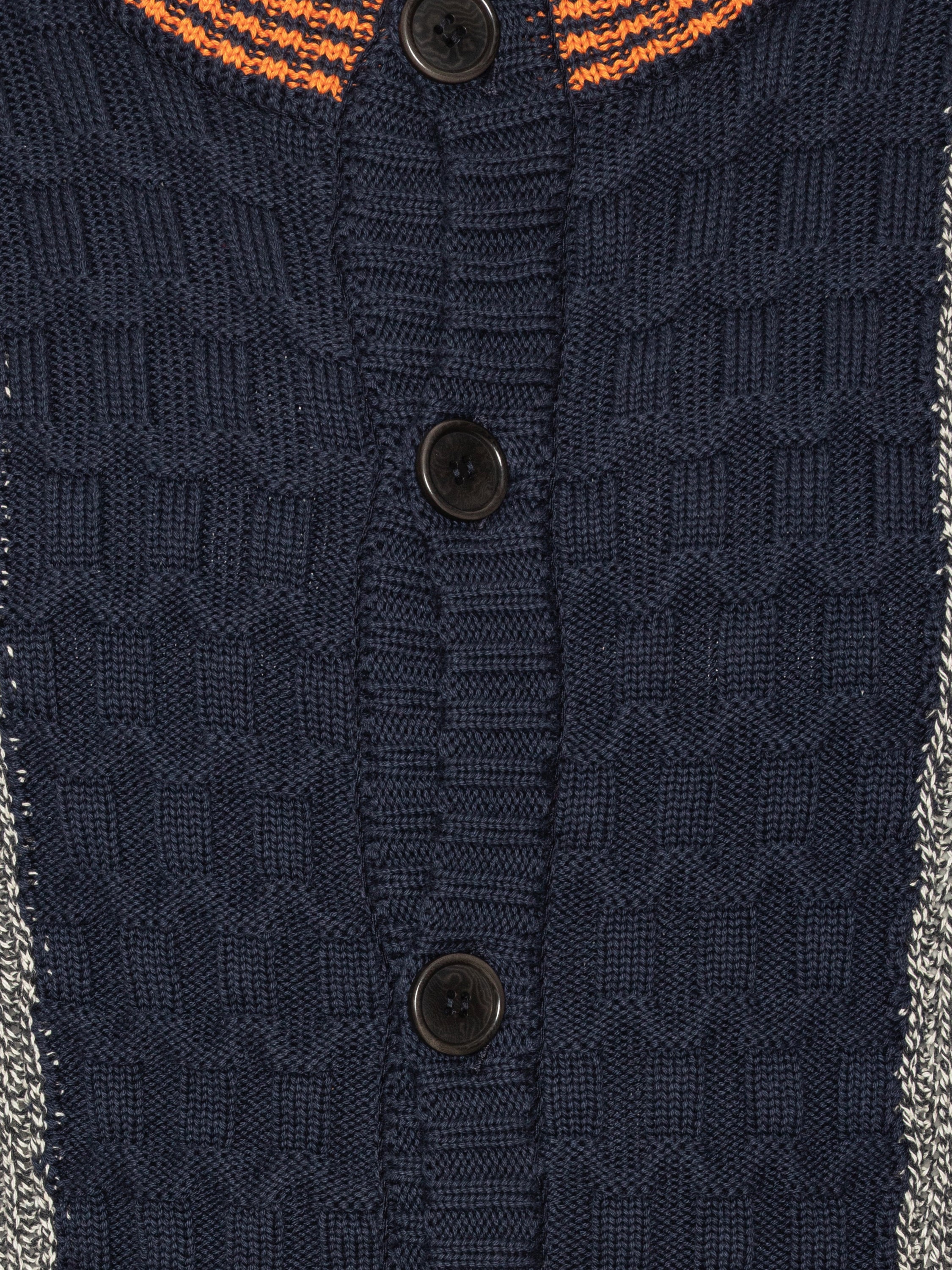 Close-up shot of the Abundance Cardigan showing the black, white, and navy block pattern, orange detailing, and textured knit fabric near the button closure