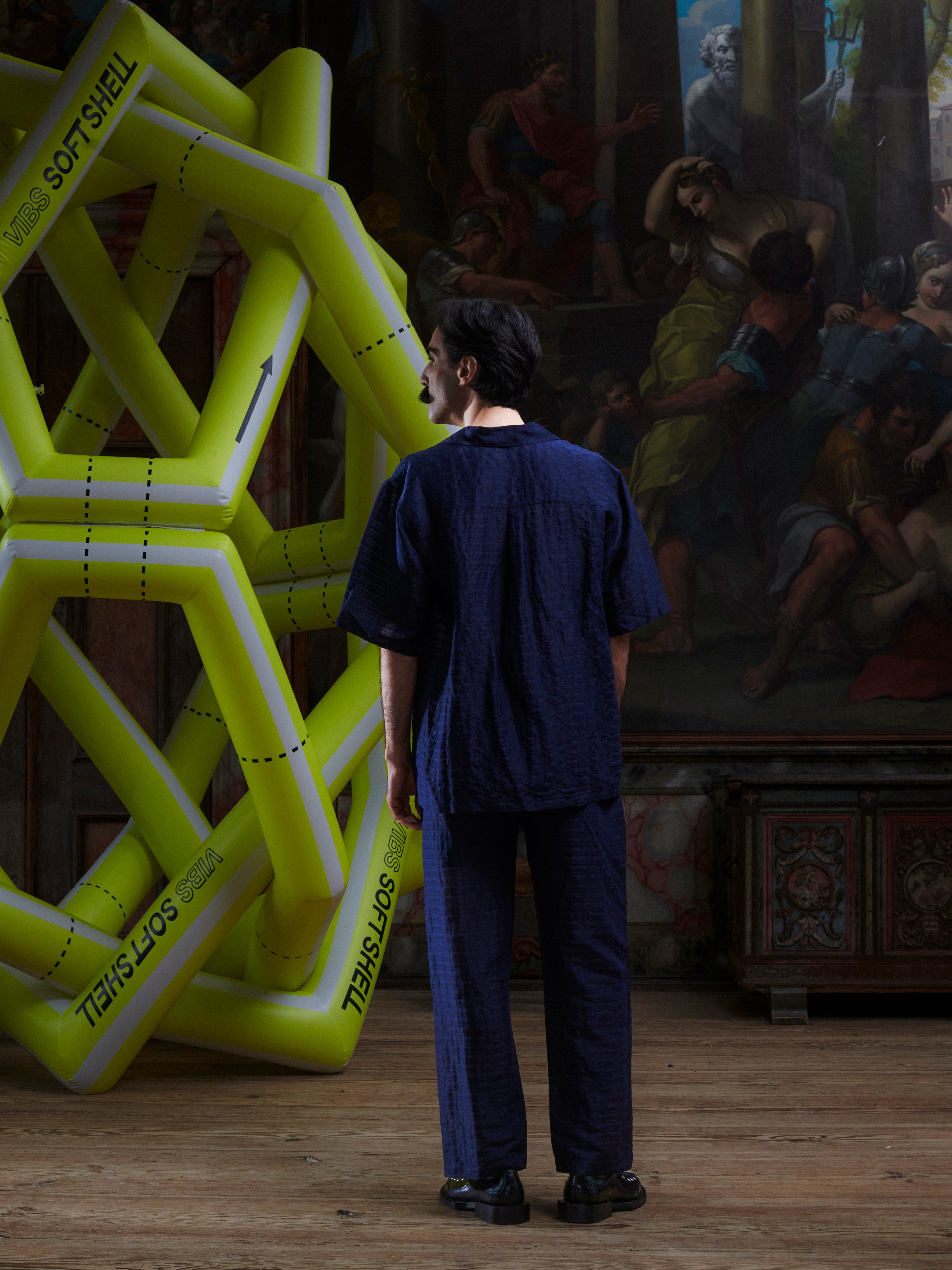 Back view of the male model wearing the Artist Pants in navy from Henrik Vibskov Spring/Summer 2026 Studio Collection, highlighting the straight-leg shape and clean back panel.