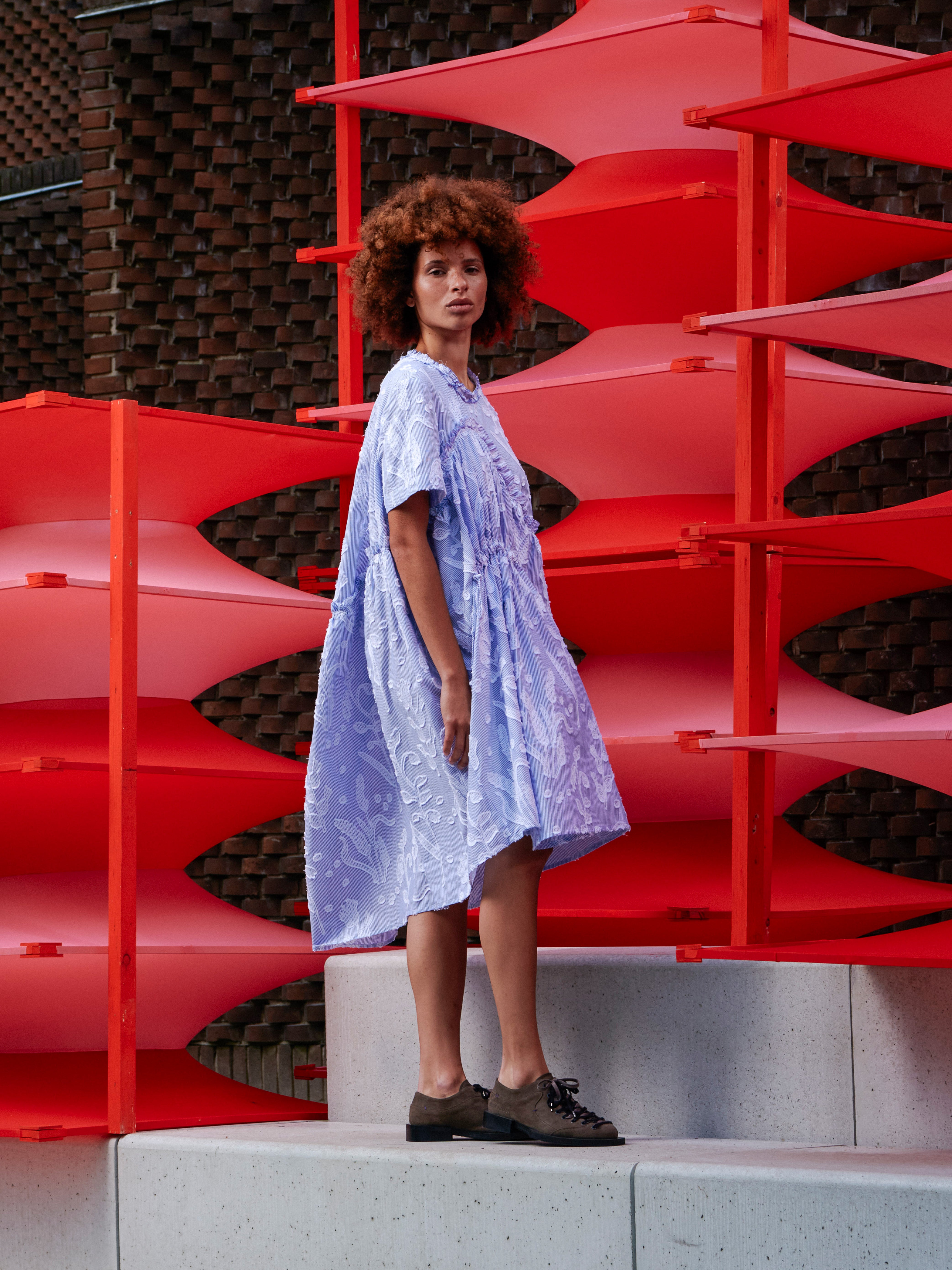 Side view of the model wearing the light blue ruched dress, highlighting the voluminous silhouette and textured floral fabric.