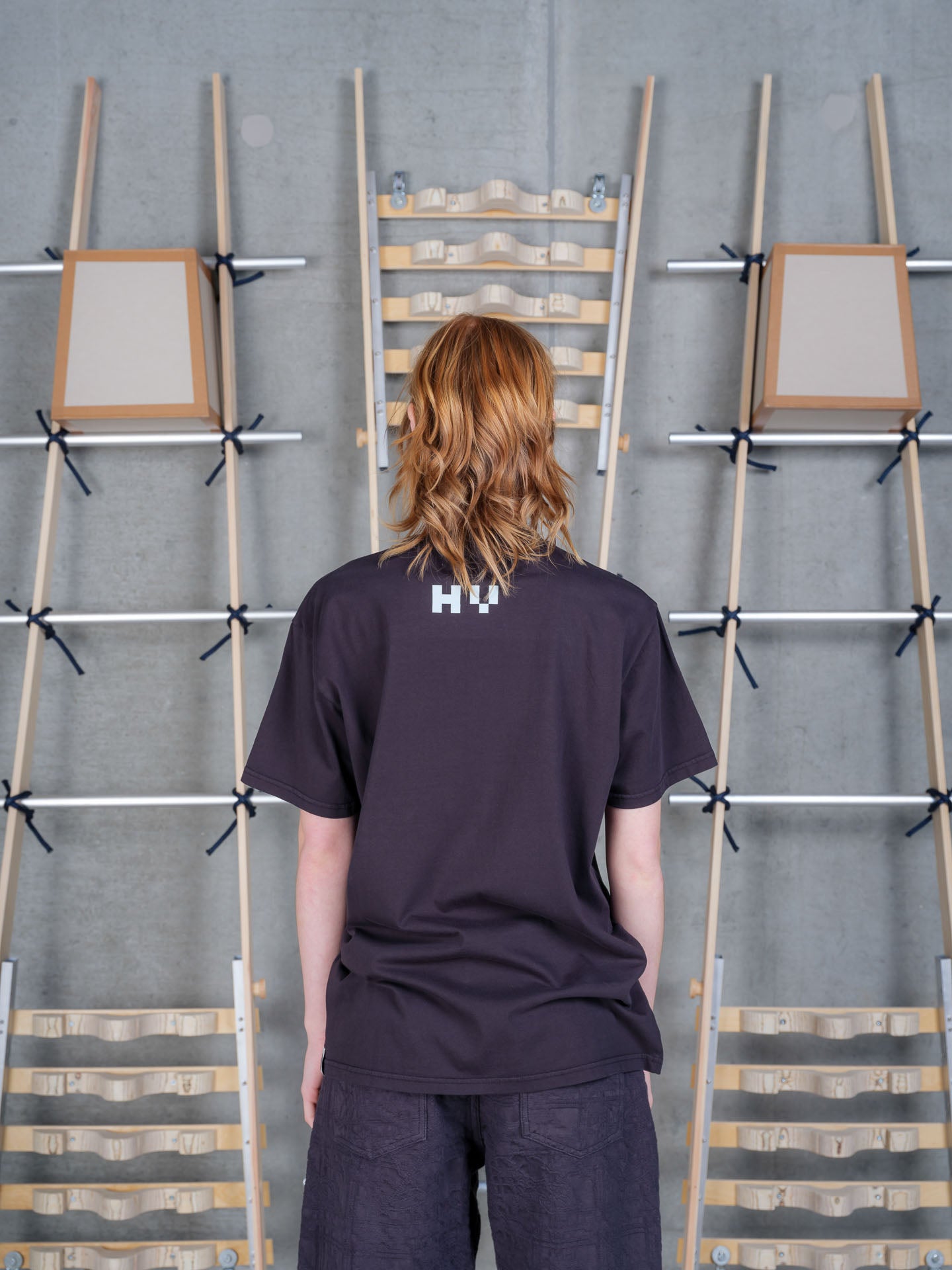 Back view of a female model wearing the Henrik Vibskov Cross Stitch Tee in Black, featuring the minimalist back, soft organic cotton construction, and easy-fitting silhouette