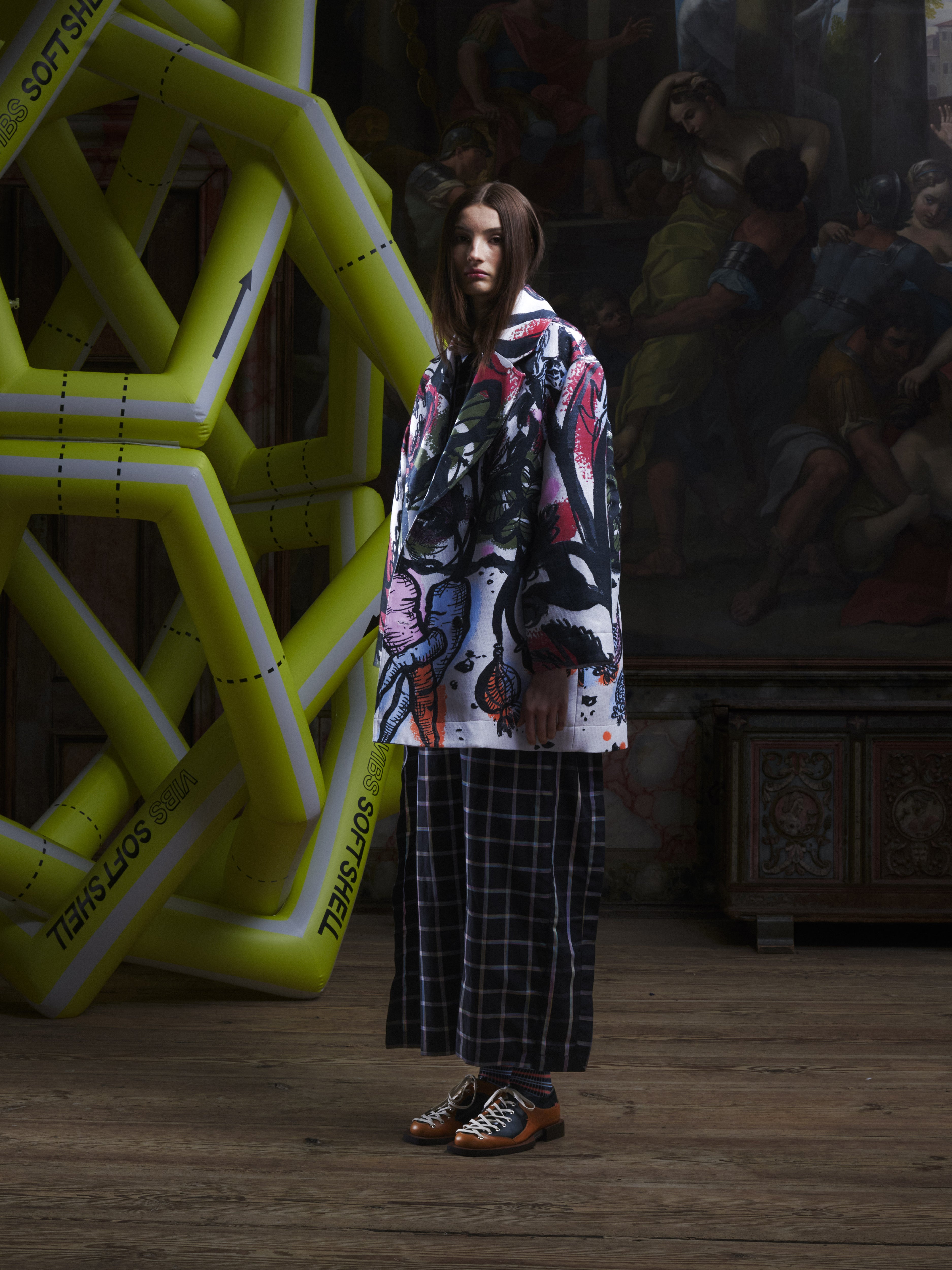 Side view of the female model wearing the Care Coat in Carrots from Henrik Vibskov Spring/Summer 2026 Studio Collection, displaying the carrot pattern, coat silhouette, and straight hem.