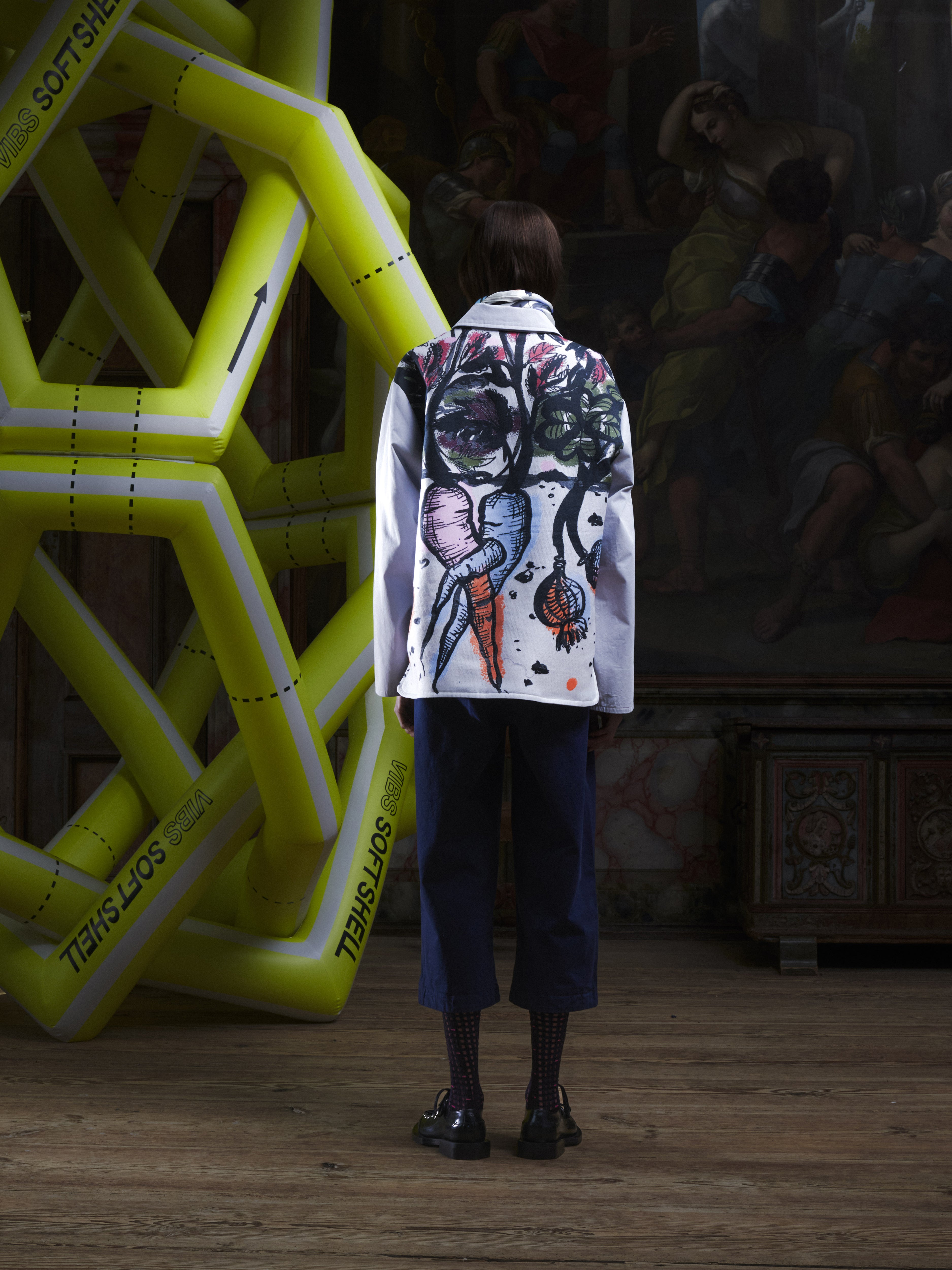 Back view of the female model wearing the Care Jacket in Carrots from Henrik Vibskov Spring/Summer 2026 Studio Collection, highlighting the full carrot-patterned design and clean straight hem.