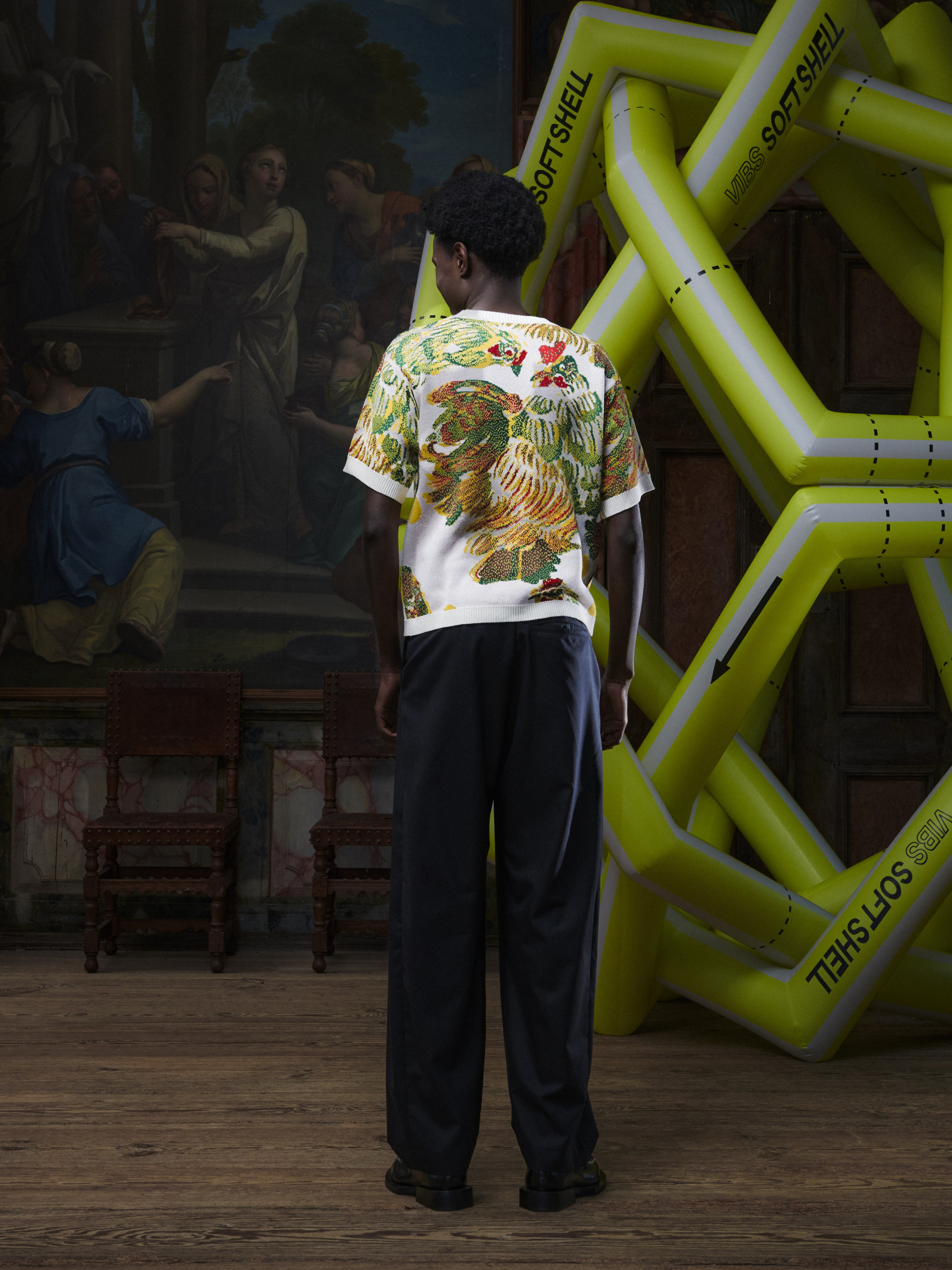Back full-body view of the male model wearing the Chicken T Knit in Chicken Ecru from Henrik Vibskov Spring/Summer 2026 Studio Collection, showing the clean back, short sleeves, and straight hem.