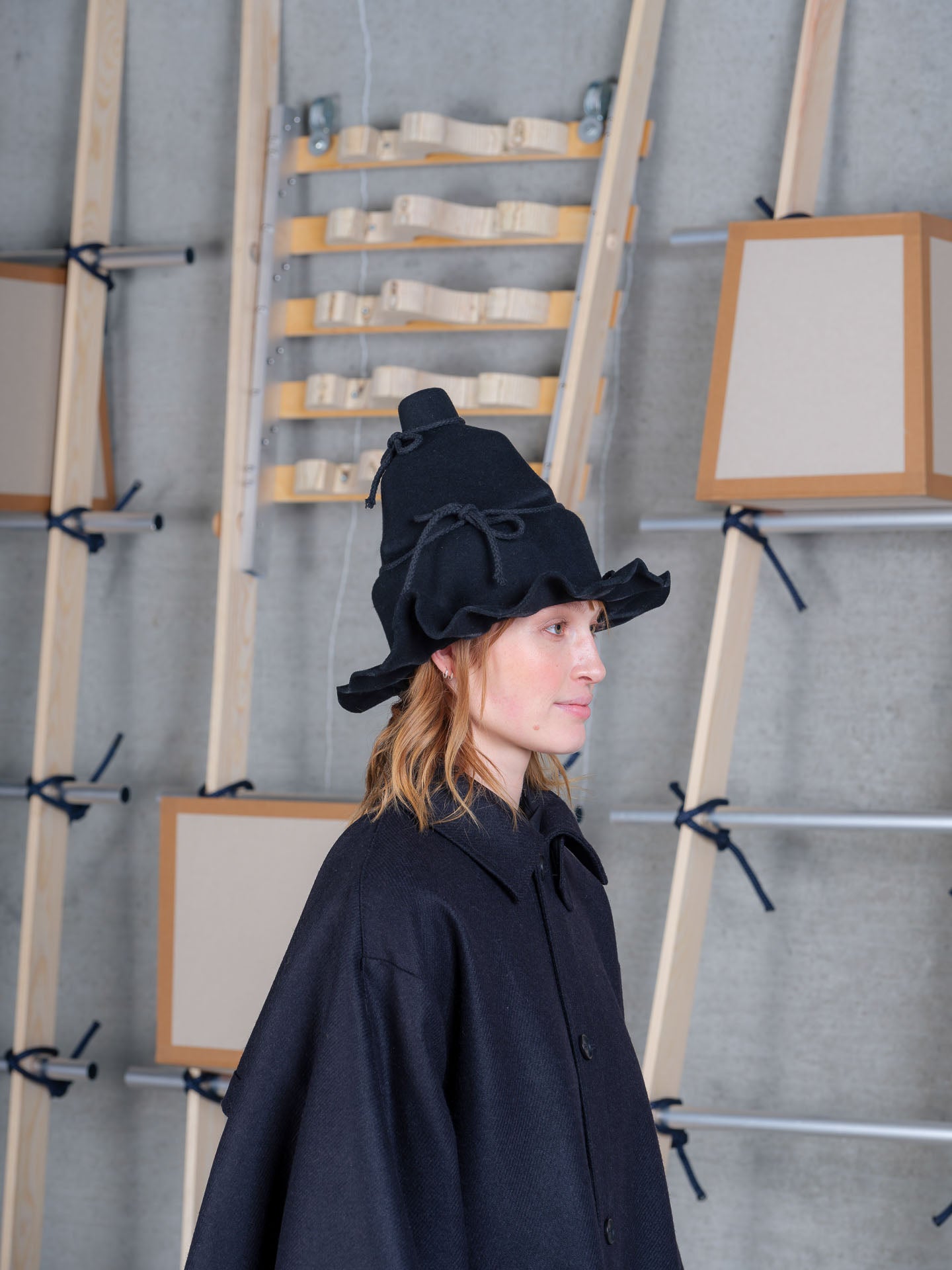 Profile view of Christo Wrap Hat by Henrik Vibskov in black wool with layered construction and textured rope ties