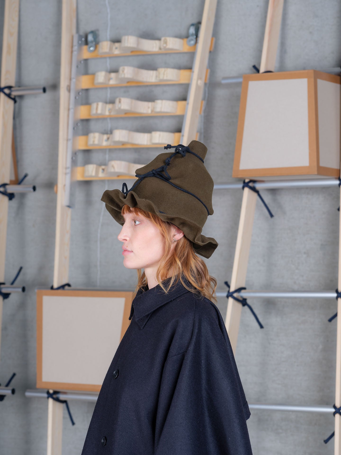 Profile view of Christo Wrap Hat by Henrik Vibskov in moss green wool with layered construction and contrast rope ties