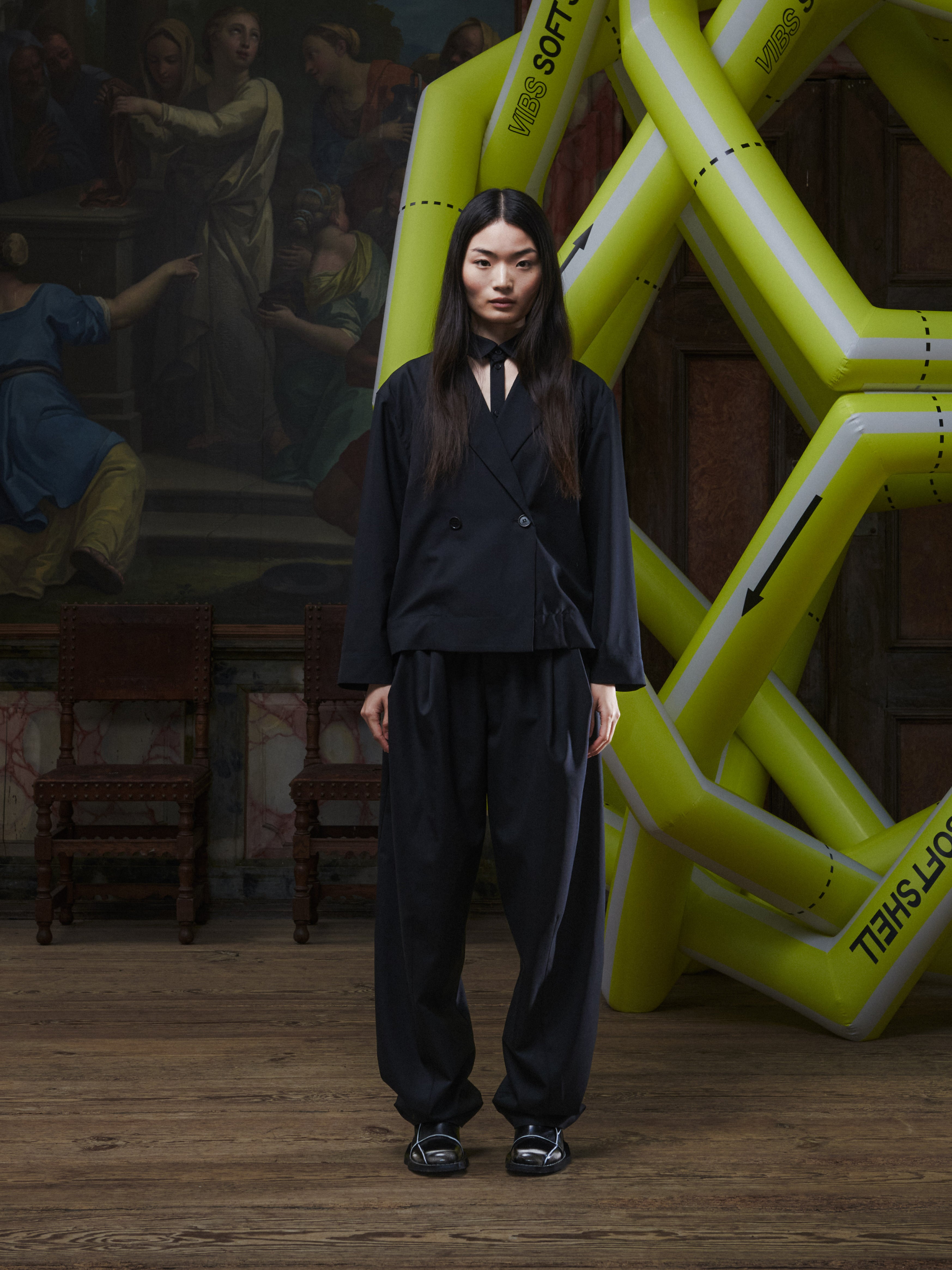 Back full-body view of a male model wearing the Claus Pants in Tropical Black from Henrik Vibskov Spring/Summer 2026 Studio Collection, showing the clean black silhouette, belt loops, and straight-leg shape.