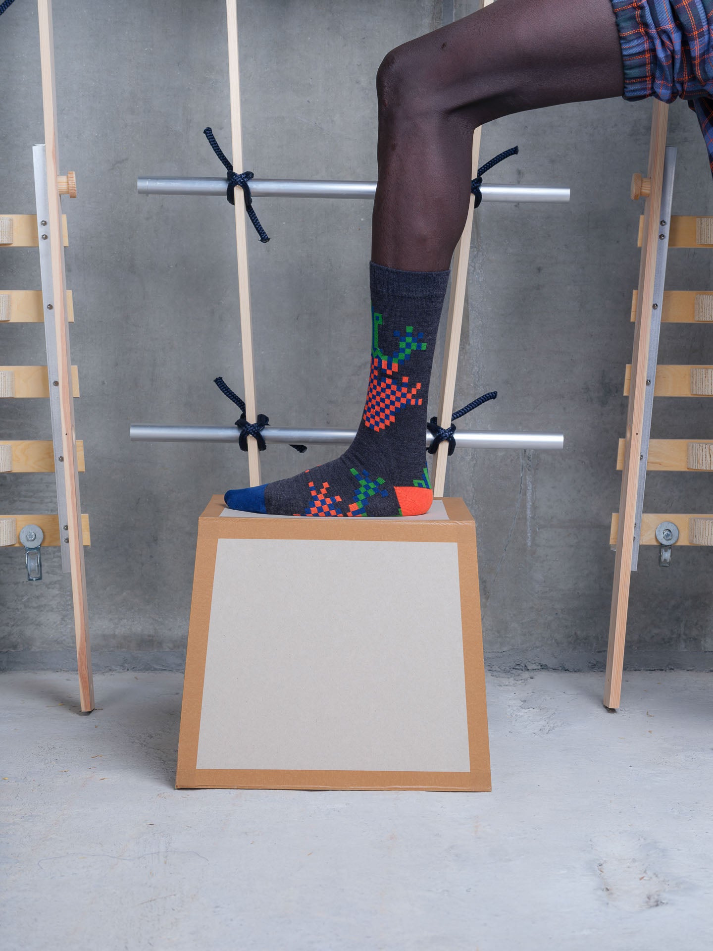 Model wearing Henrik Vibskov Cross Stitch Sock in pixelated black frog with checkerboard motif, contrast heel and blue toe