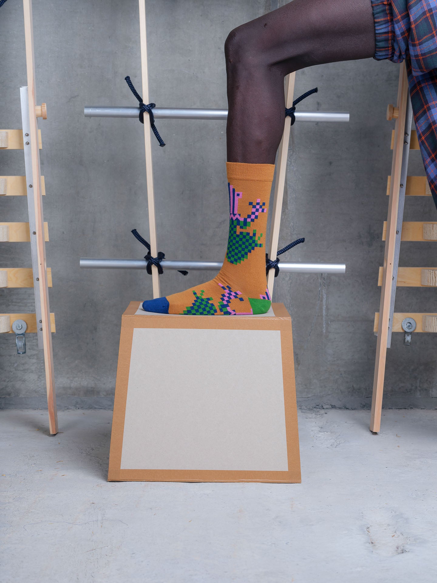 Model wearing Henrik Vibskov Cross Stitch Sock in pixelated spice frog with checkerboard motif, contrast green heel and navy toe
