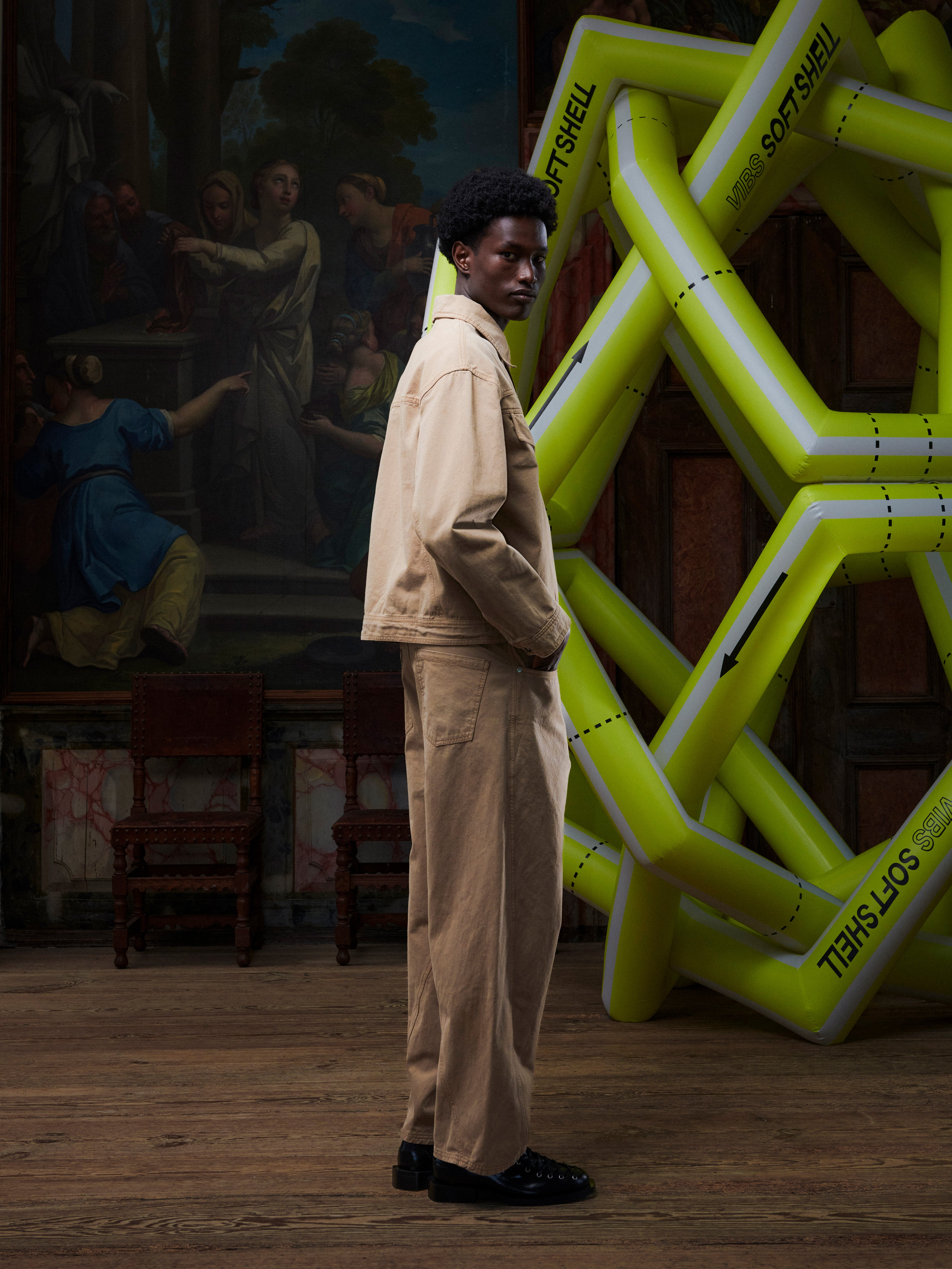 Side view of the male model in the Curved Denim Pants, showing the side pockets, leg shape, and dark beige denim. Model is 191cm tall and wears size M.