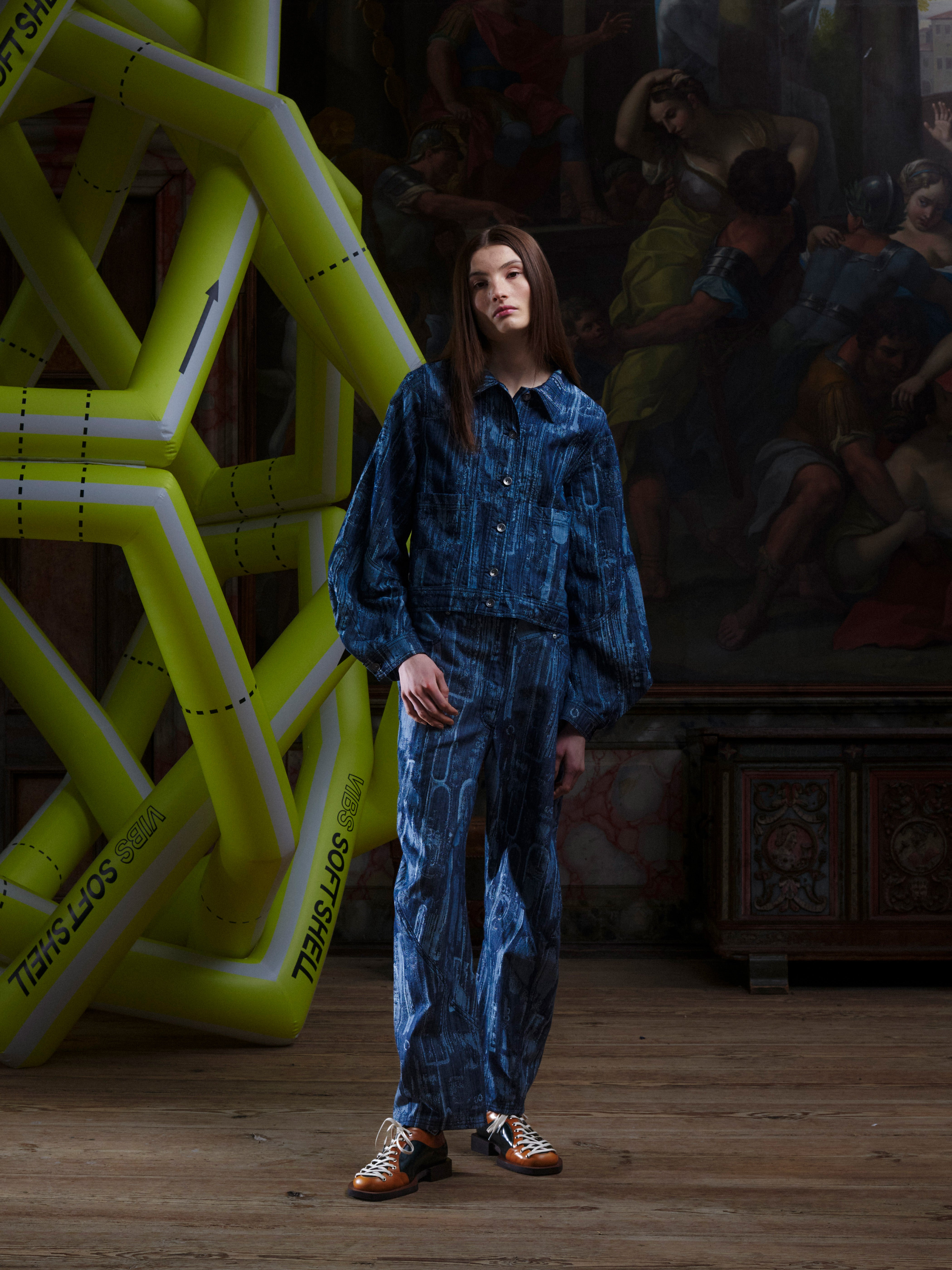 Female model wearing the Curved Denim Pants from the front, displaying the relaxed straight-leg fit in size L and the grey-blue instrument-patterned denim. Model is 185cm tall and wears size L.