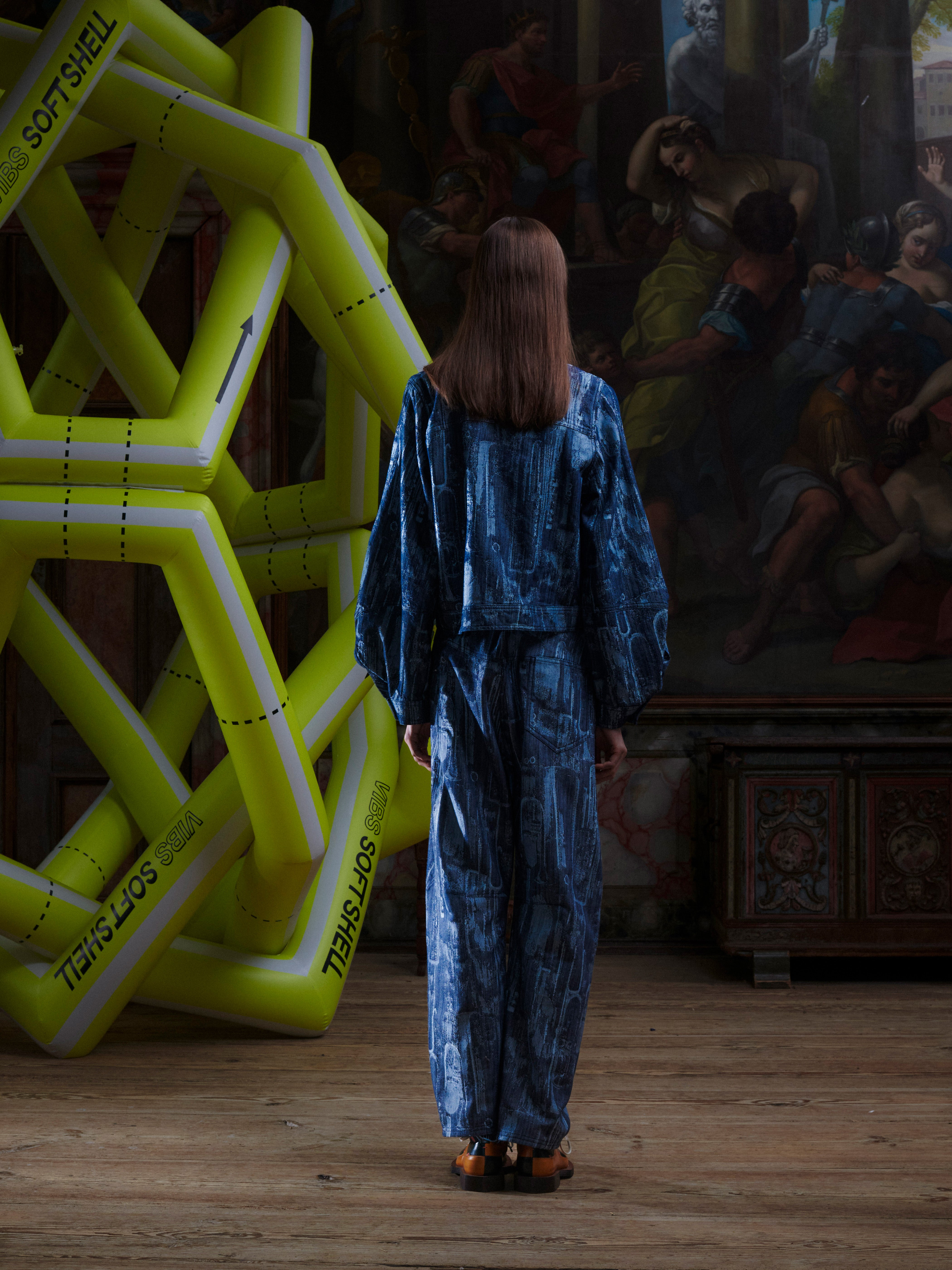 Back view of the female model in the Curved Denim Pants, showing the back pockets, straight silhouette, and instrument-patterned denim. Model is 185cm tall and wears size L.