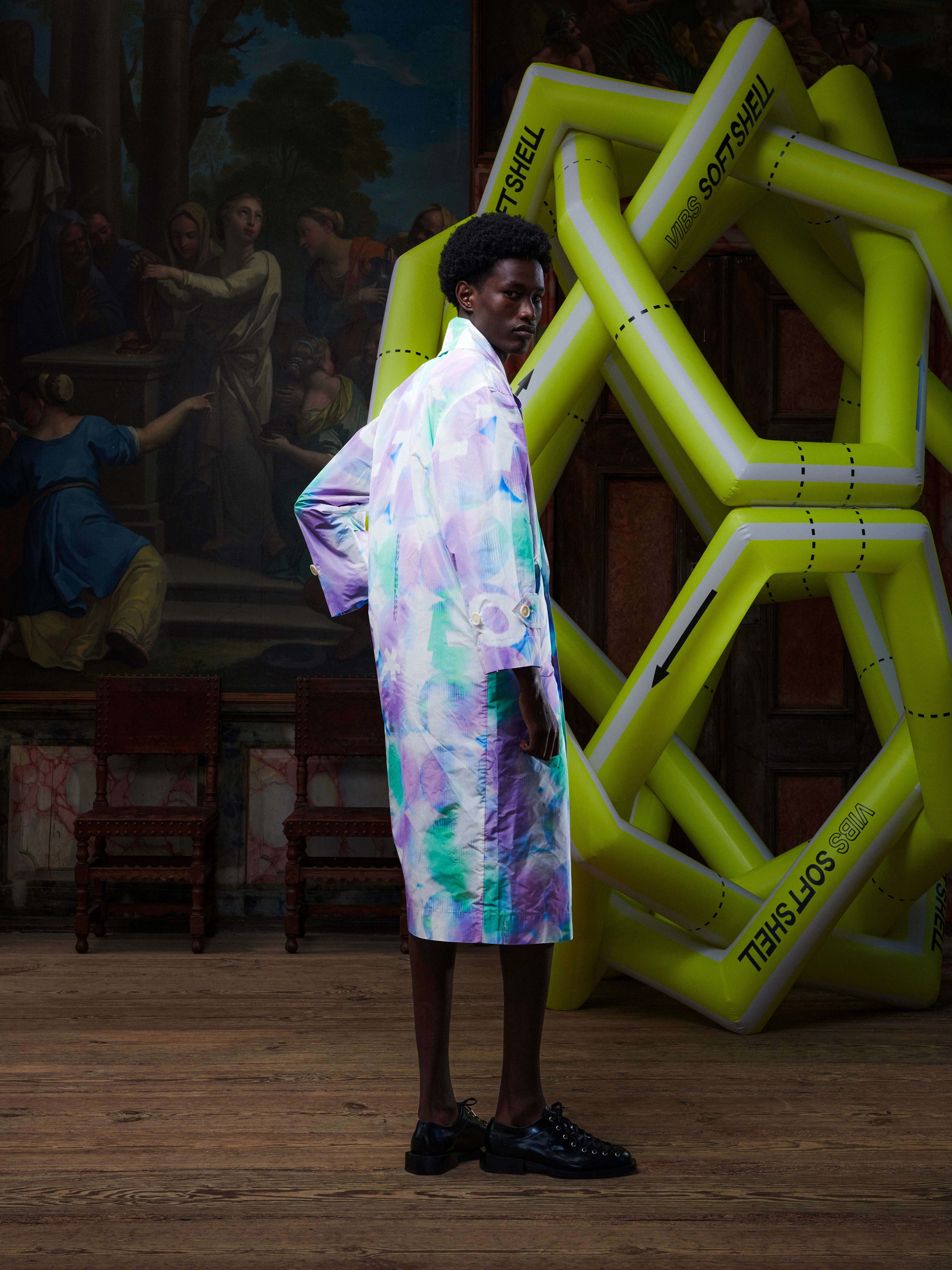 Side view of model wearing the Dimout Long Coat in Bubble Wrap, showing the long relaxed fit, side pocket placement, and multicolour abstract design.