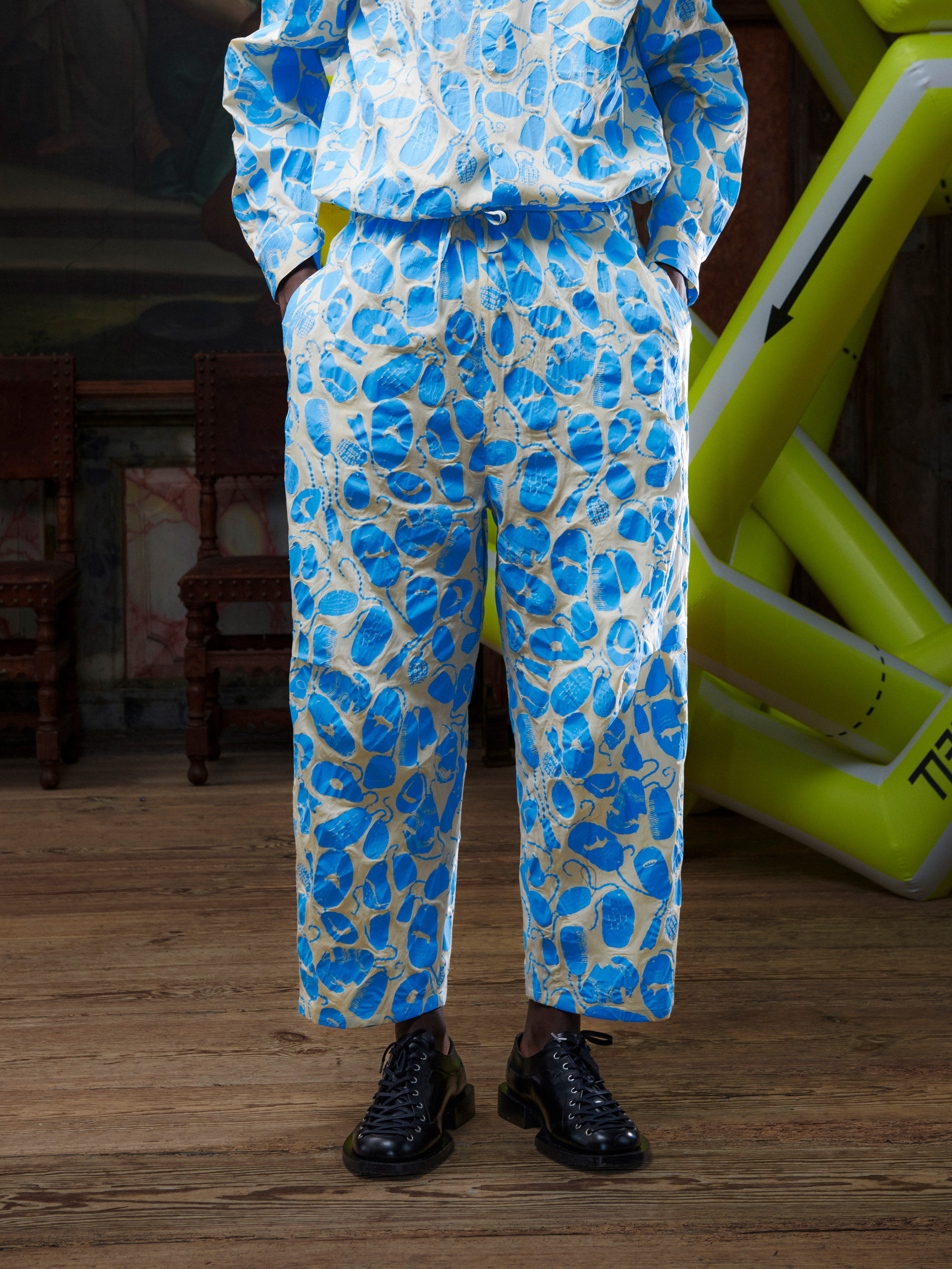 Close-up front view of male model wearing the Drawstring Pants in Ecru Amulets, showing the waistband, drawstring, and blue amulets pattern. Model is 191 cm and wears size XS.