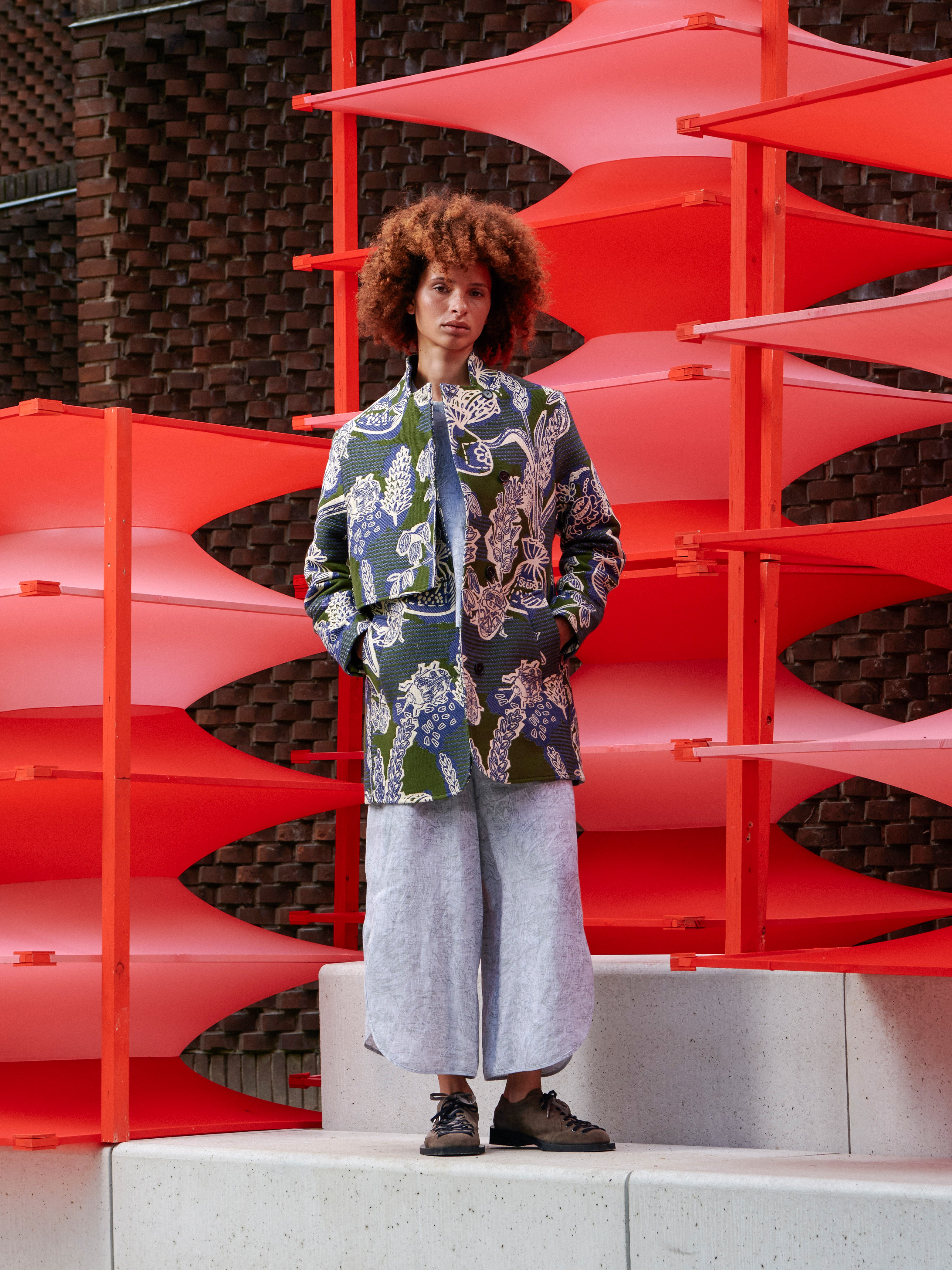 Side view of the model wearing the floral coat, highlighting the layered silhouette and fluid drape.