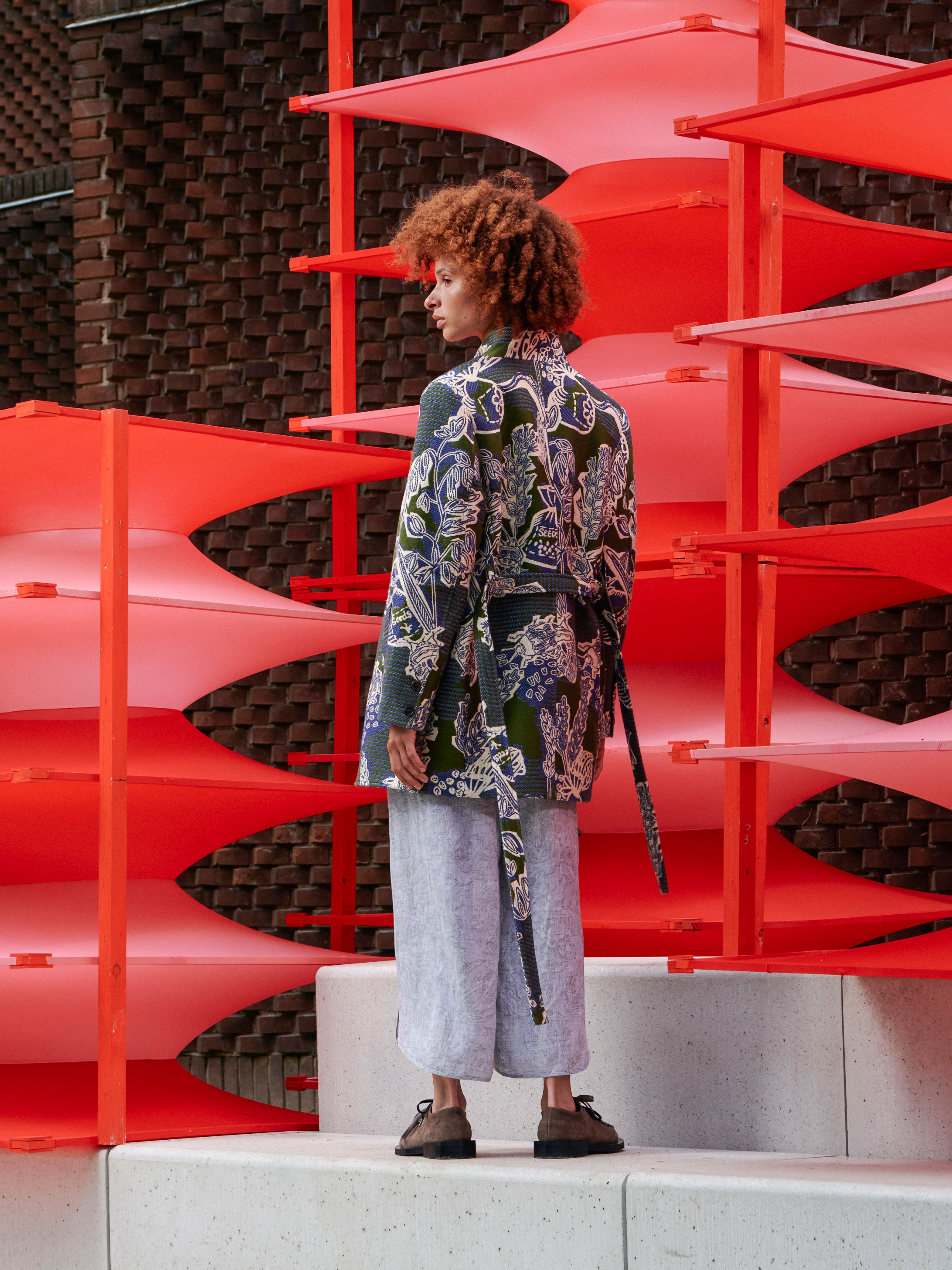 Back view of the model wearing the Garden of Eeden coat, showcasing the statement print and adjustable waist detail.