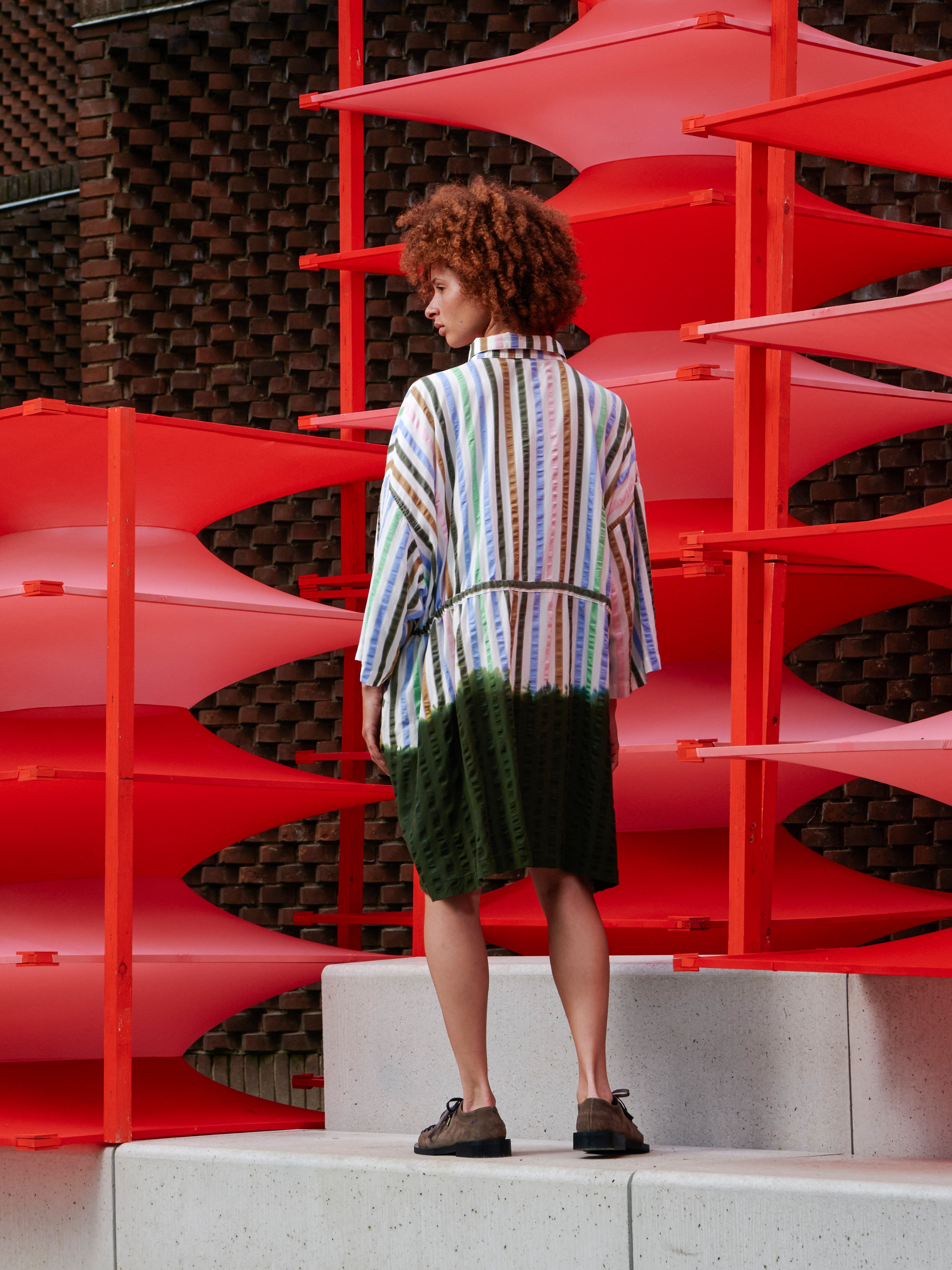 Back view of the model wearing the multicolour striped Gather Dress, showcasing the relaxed silhouette and green dip dye effect.