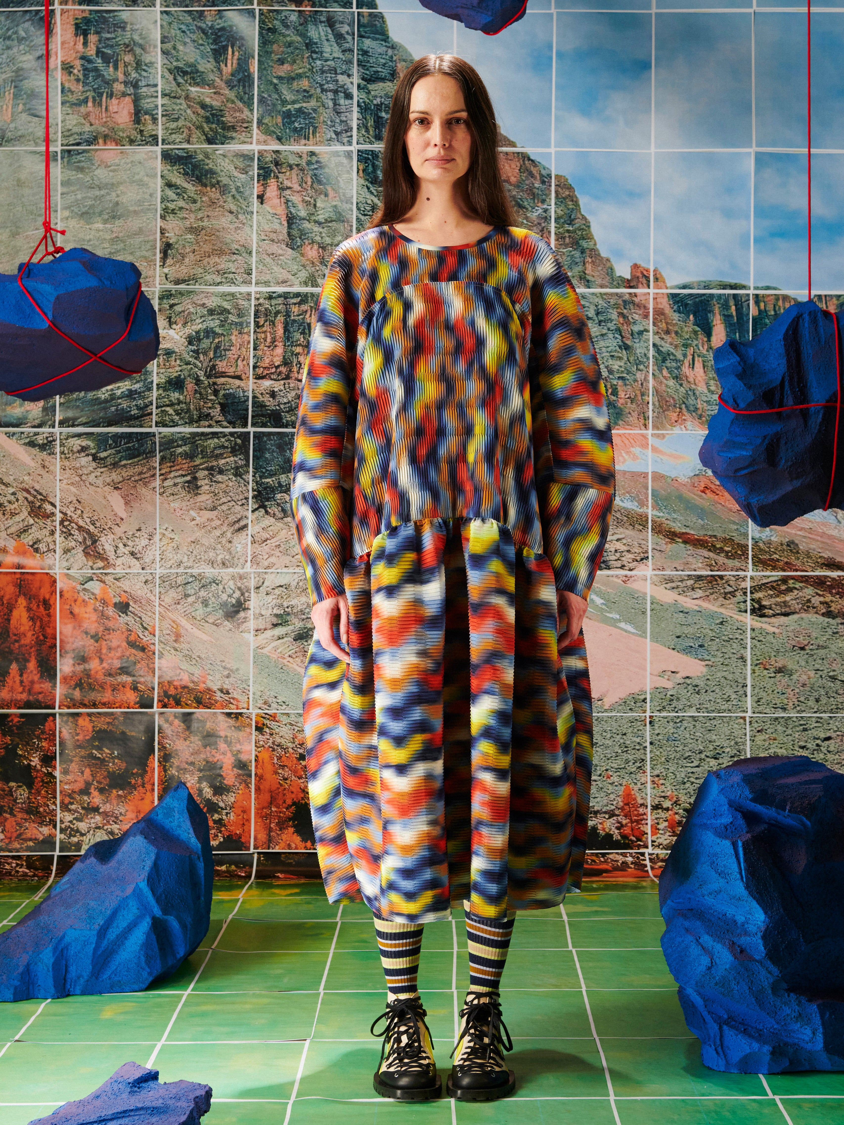 Person wearing a colorful dress from Henrik Vibskov standing in front of a tiled wall with abstract patterns