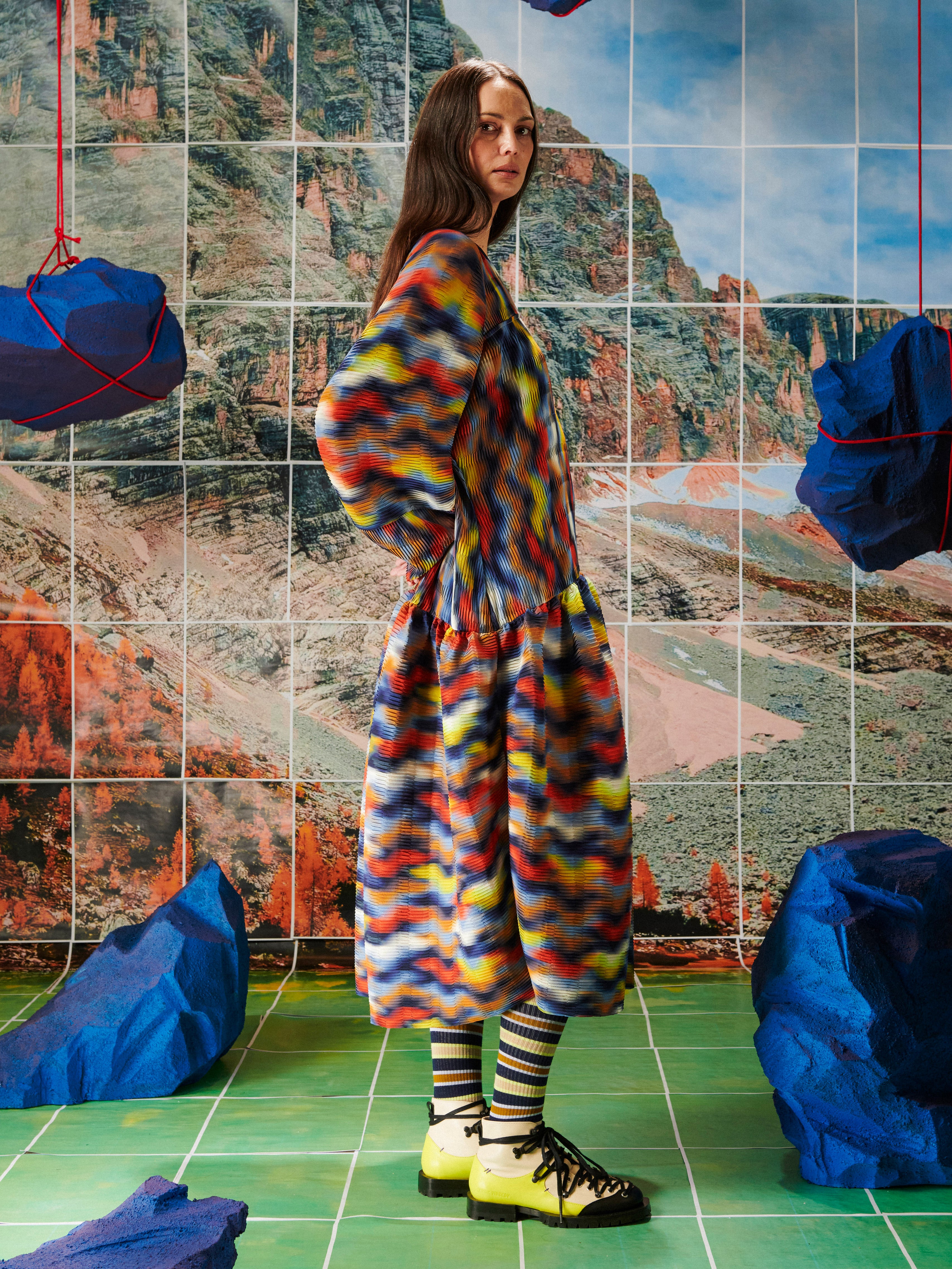 Person wearing a colorful dress from Henrik Vibskov standing in front of a tiled wall with abstract patterns