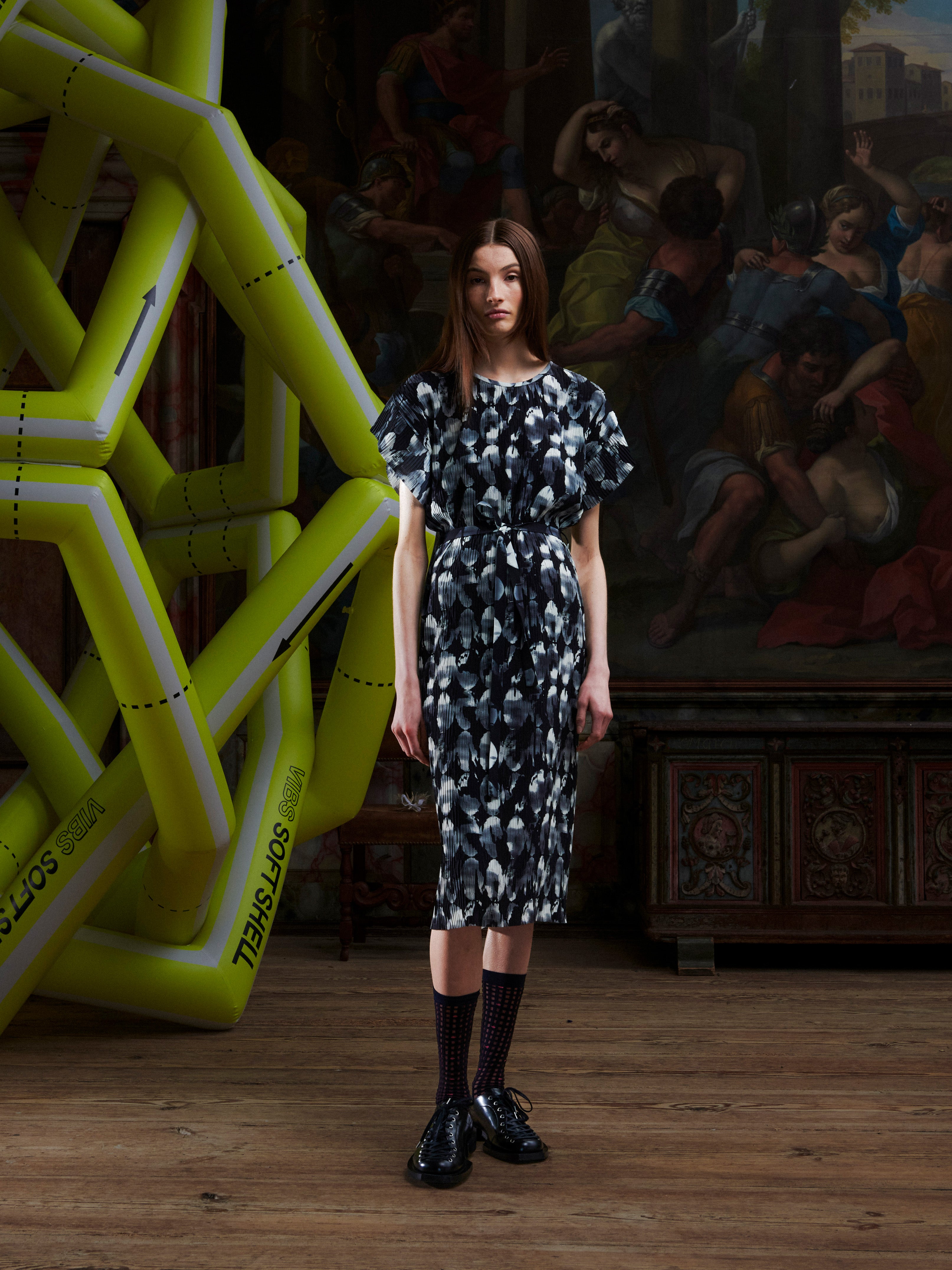 Model wearing the Henrik Vibskov New Pina Plissé Dress in Bursting Eggs, front view. The model is 185 cm and wears size S, showing the round neck, short sleeves, waist tie, and plissé fabric with abstract egg print.
