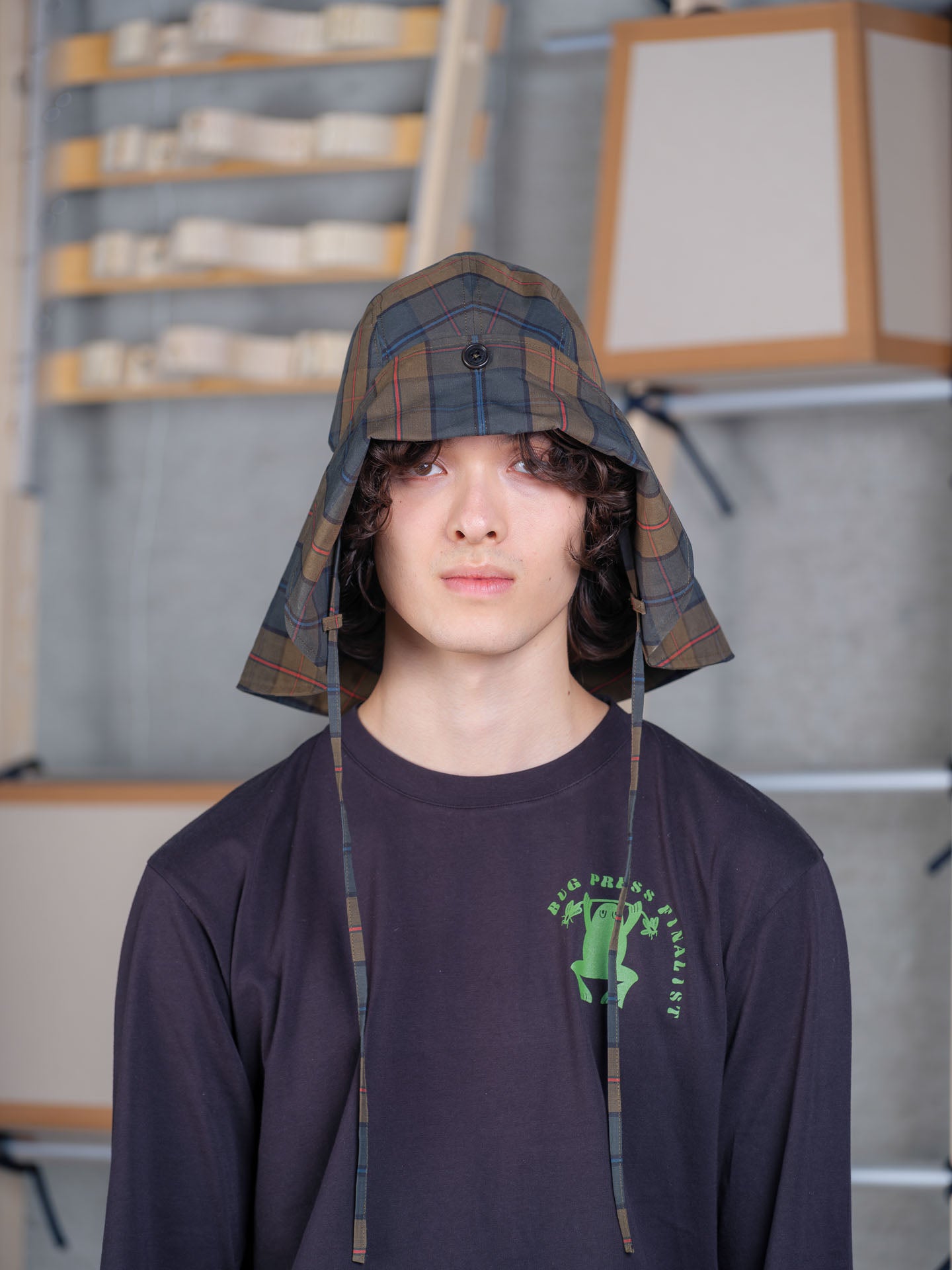 Model wearing Henrik Vibskov Nilsson Fisherman Hat in tartan with wide brim, chin straps and dry wax finish