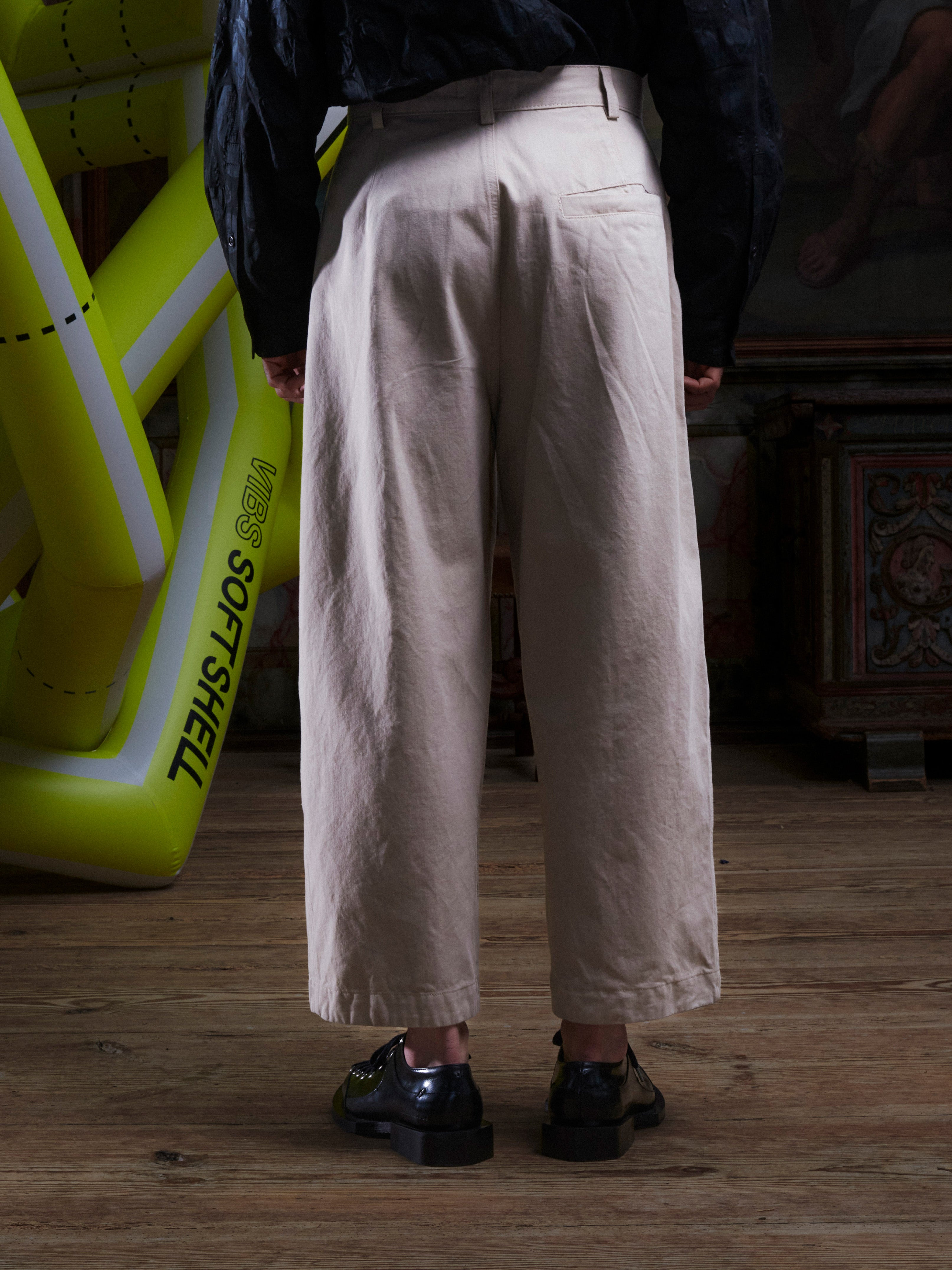 Close-up of the male model wearing the Henrik Vibskov Open Dart Pants in sand beige, back view, showing the waistband, belt loops, and rear construction.