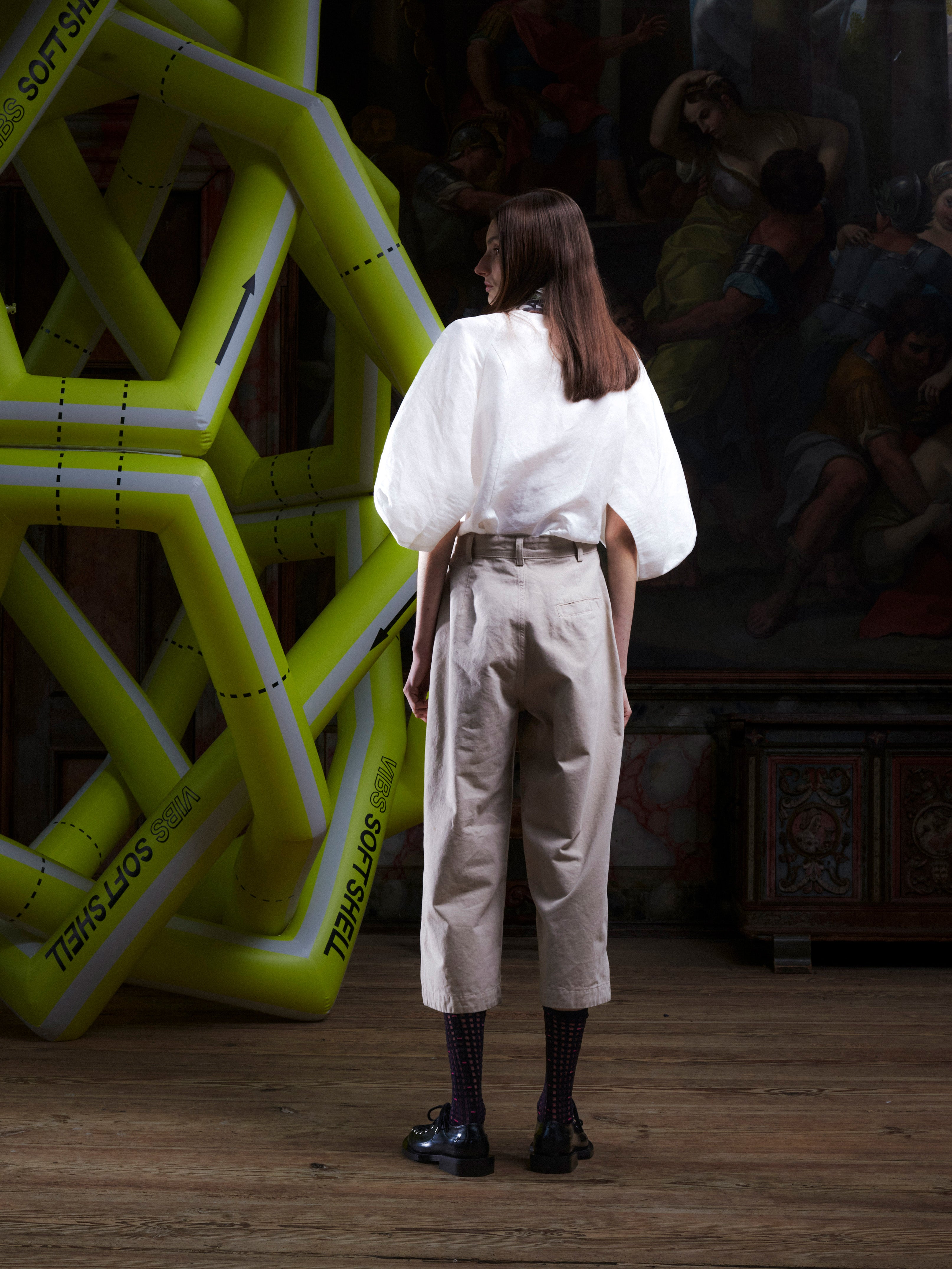 Female model wearing the Henrik Vibskov Open Dart Pants in sand beige, back view, showing the clean back, belt loops, and wide, cropped leg shape.