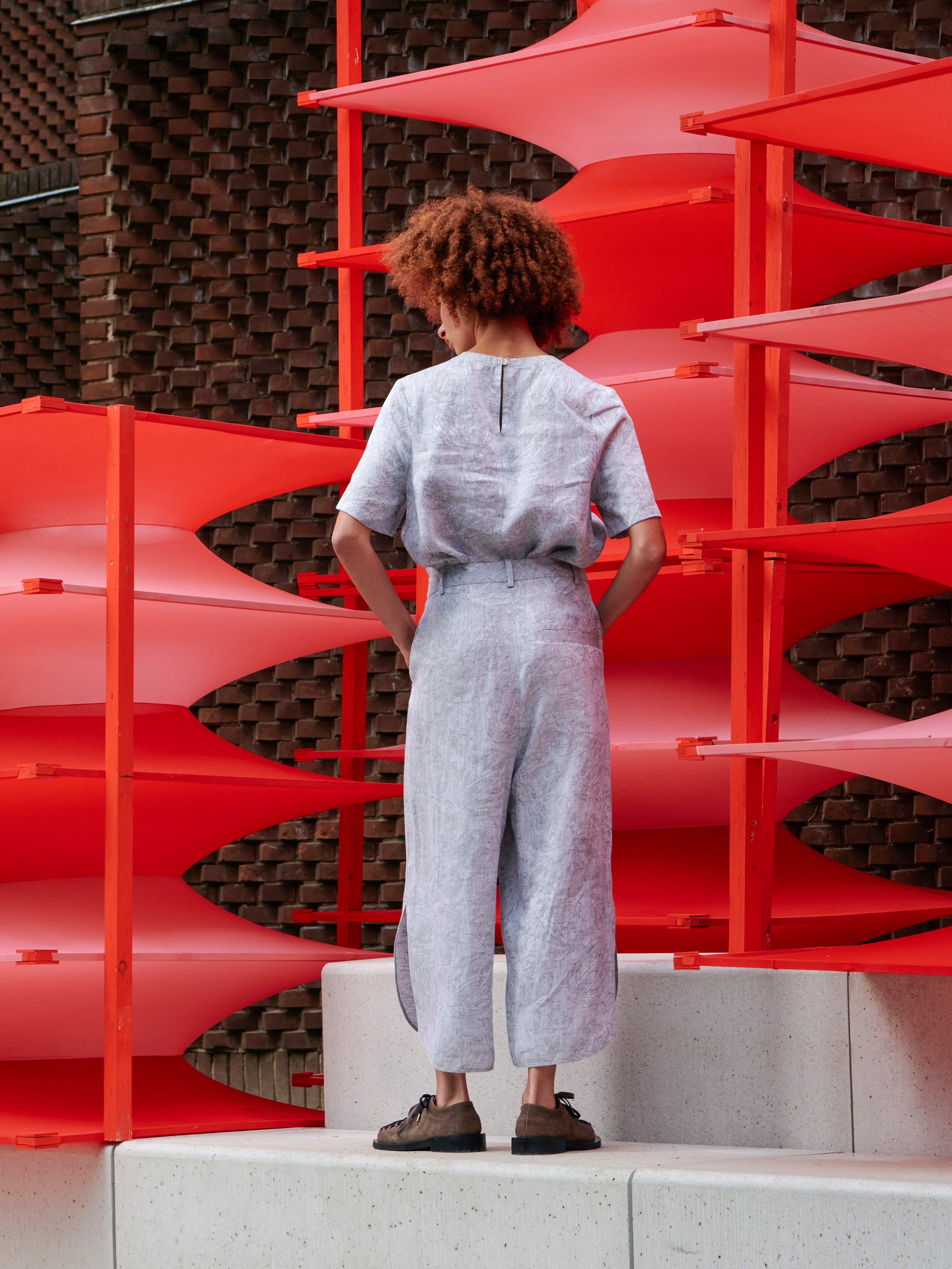 Back view of the model wearing Overlap Pants, showing the wide-leg shape, side pockets, and textured fabric detail.