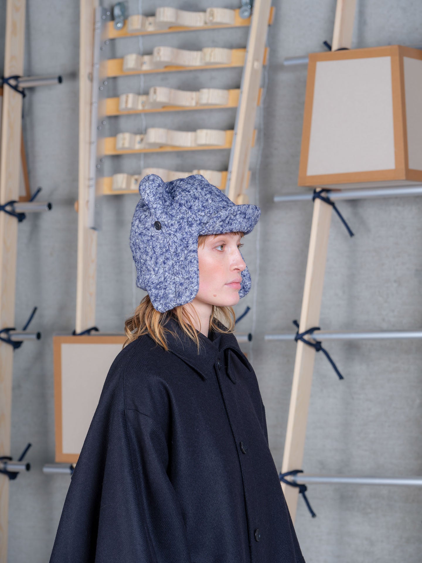 Female model wearing Henrik Vibskov blue pebbles Pilot Frog Hat with oversized navy outerwear and sculptural cotton hat silhouette