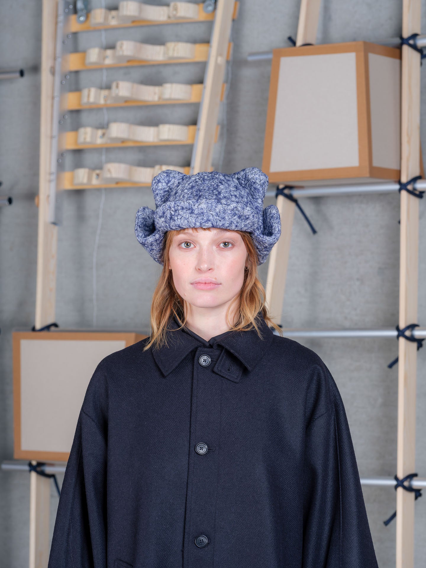 Female model wearing Henrik Vibskov Pilot Frog Hat in blue pebbles with textured mottled finish, rounded crown and folded side flaps
