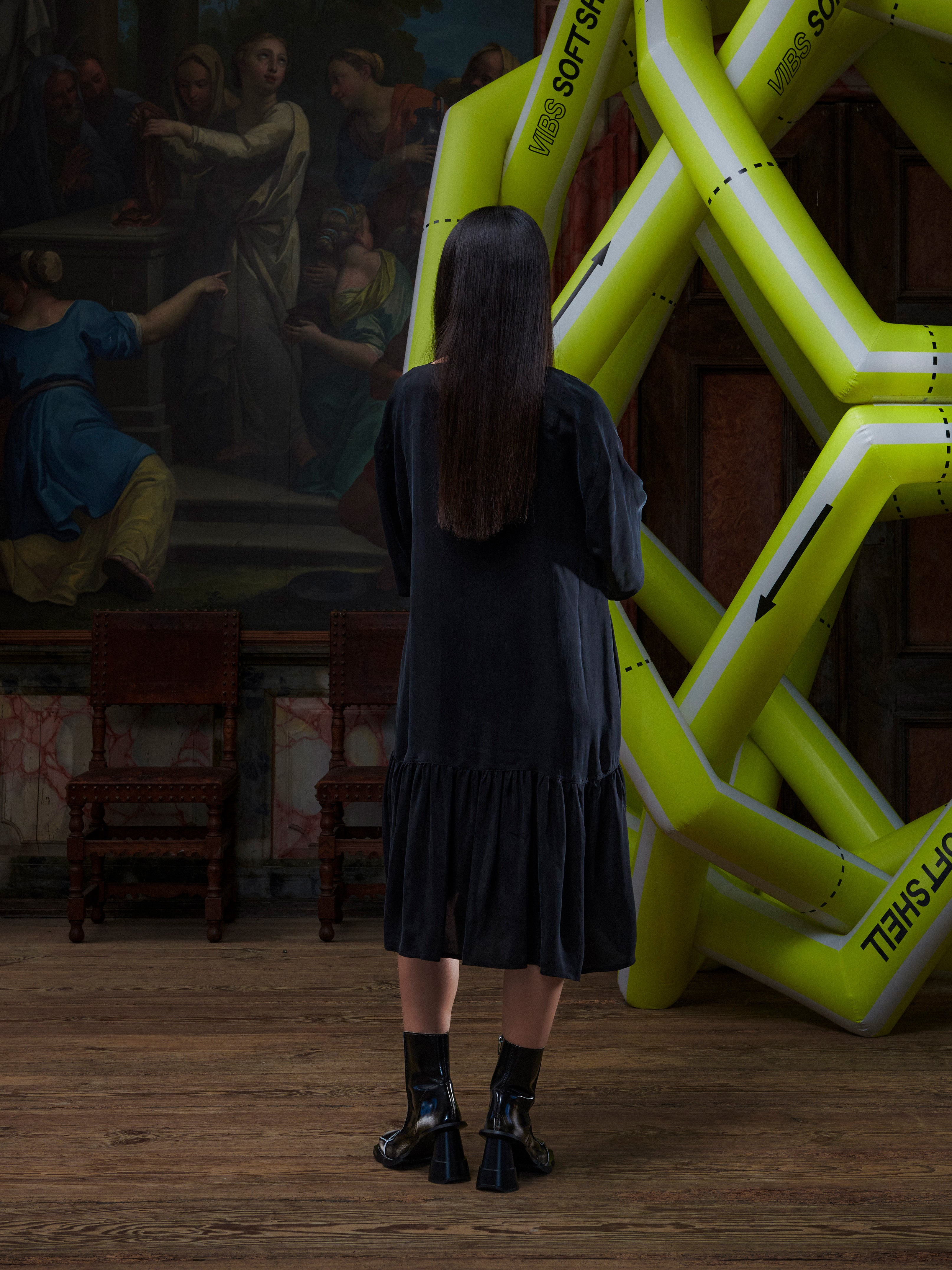Model wearing the Henrik Vibskov Preserve Dress in black, back view, showing the straight hem and loose, minimal silhouette.