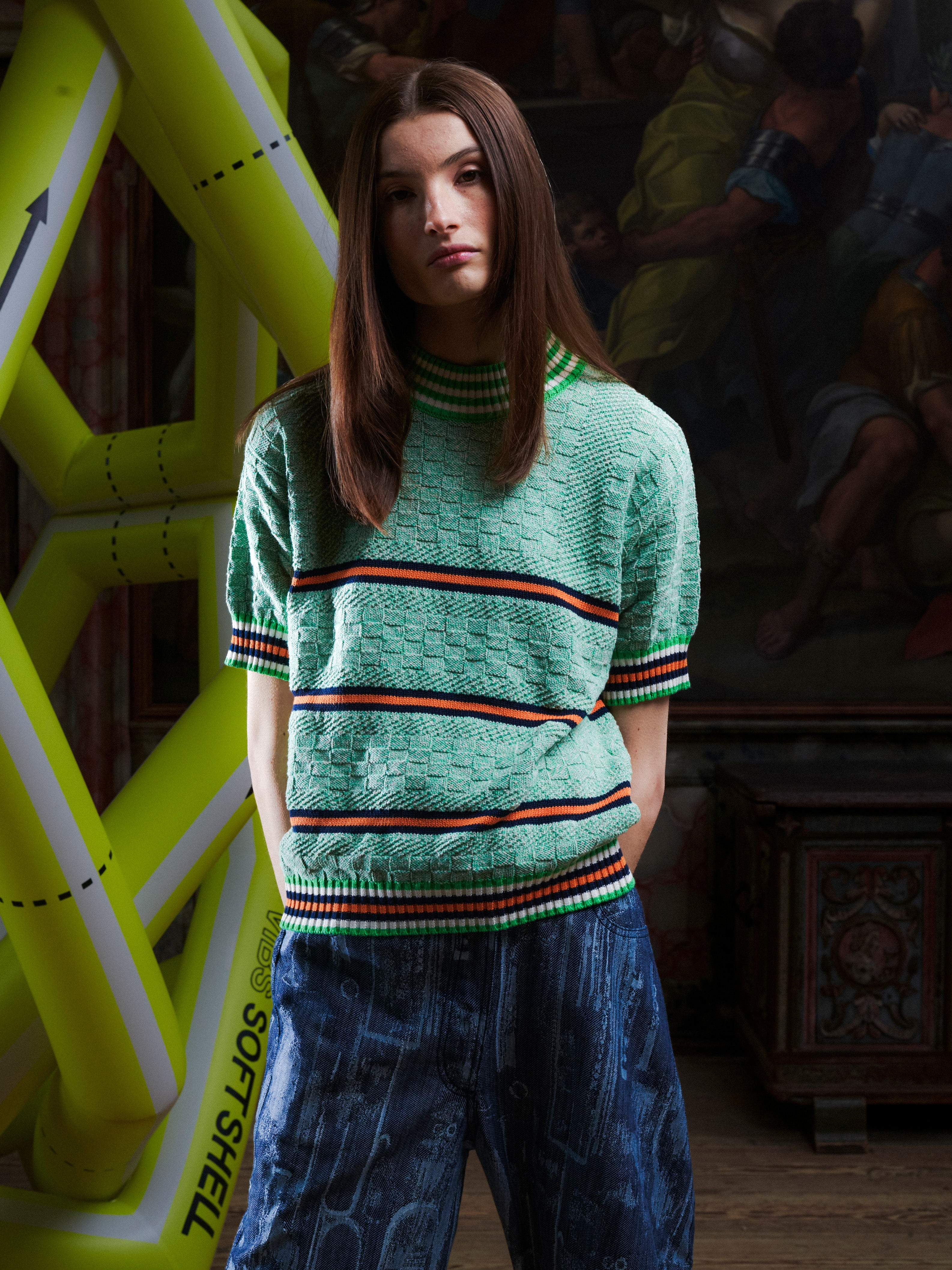 Woman wearing the mint green knitted top with stripe details from Henrik Vibskov with a yellow inflatable sculpture in the background.