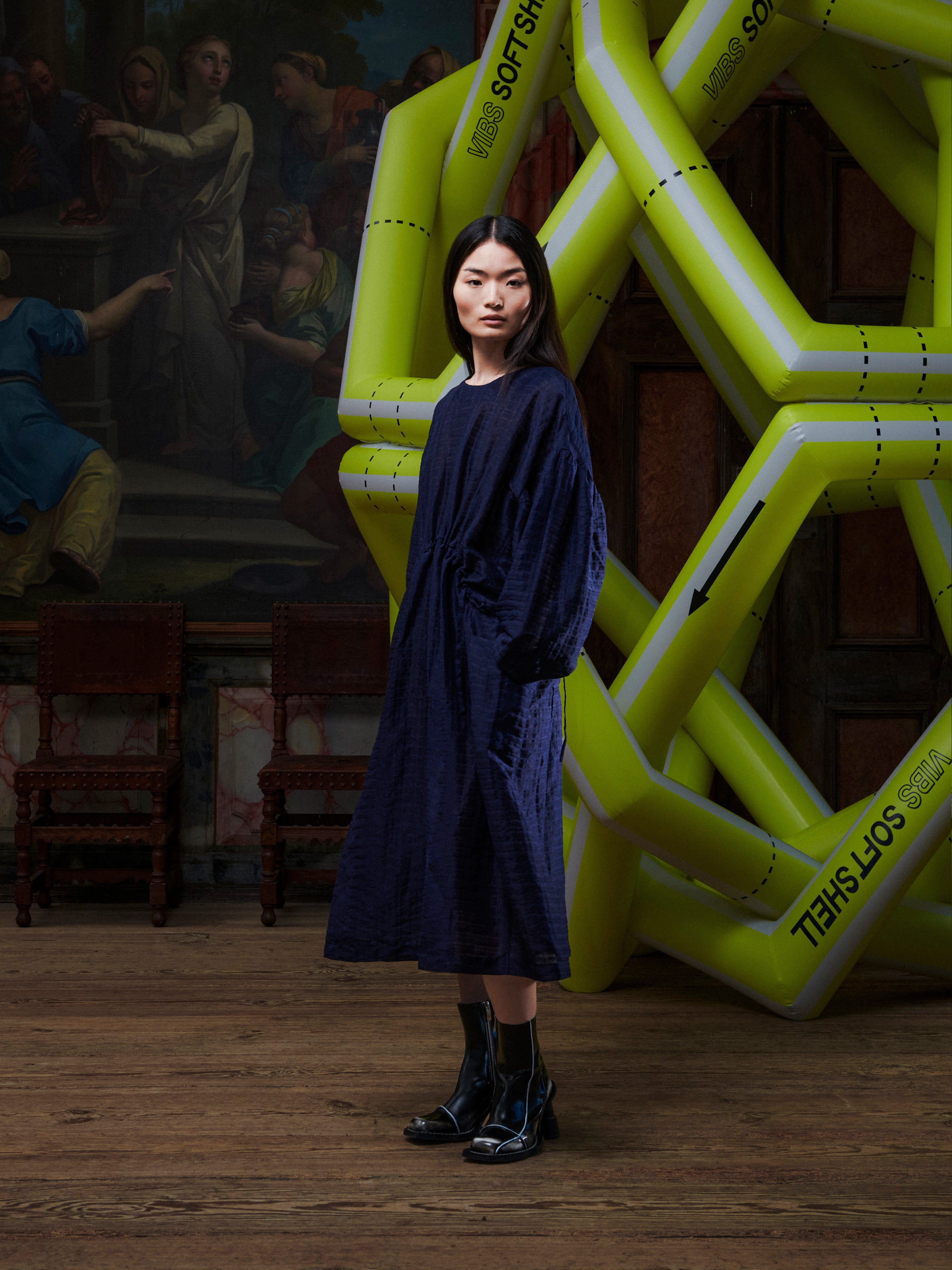 Side profile of the woman wearing the navy long sleeve dress from Henrik Vibskov in front of a yellow inflatable sculpture.
