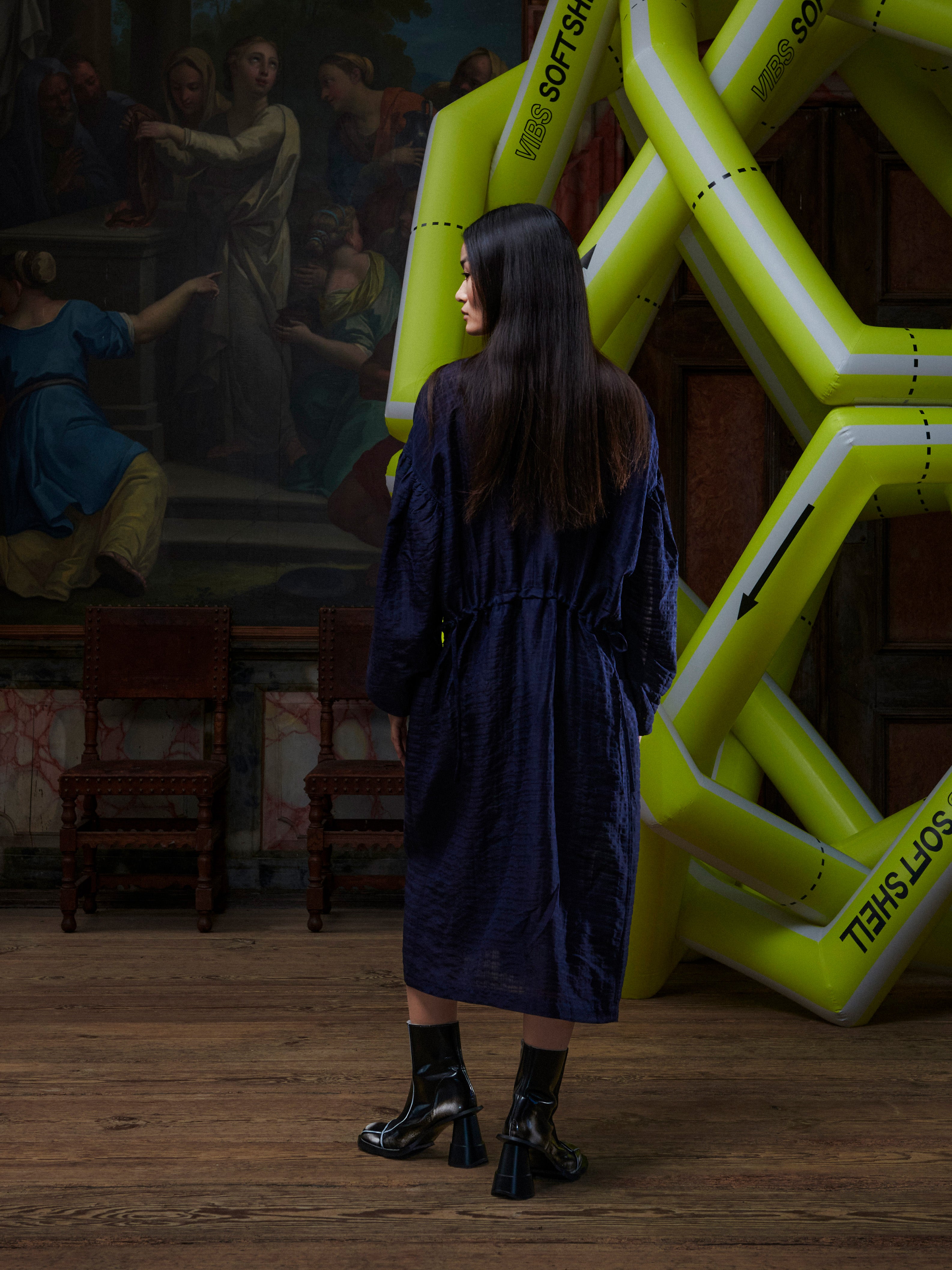 Back view of the woman wearing the navy long sleeve dress from Henrik Vibskov in front of a yellow inflatable sculpture.