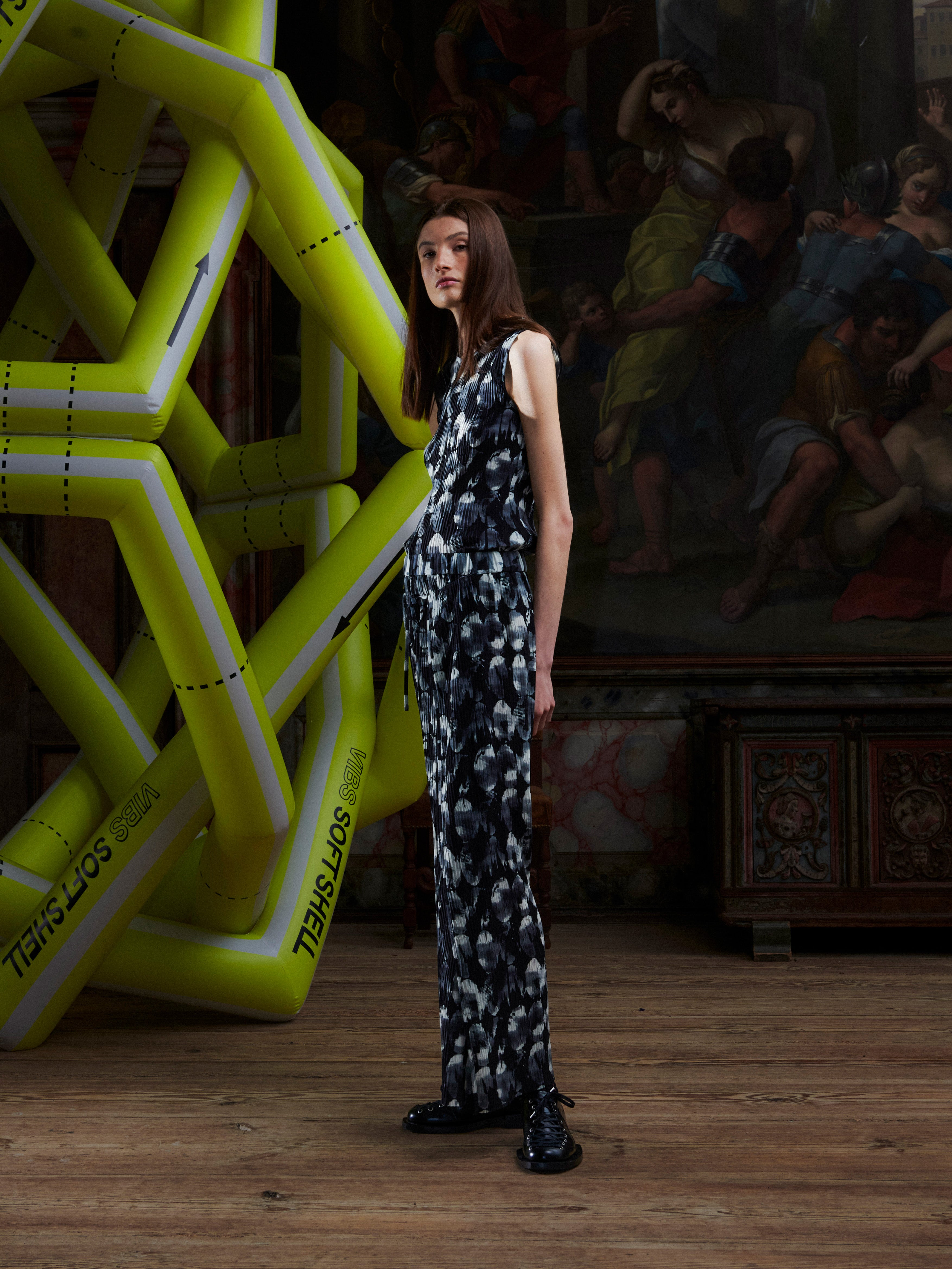 Side profile of woman in a black and white patterned top and pants standing in front of a large inflatable sculpture and artwork.