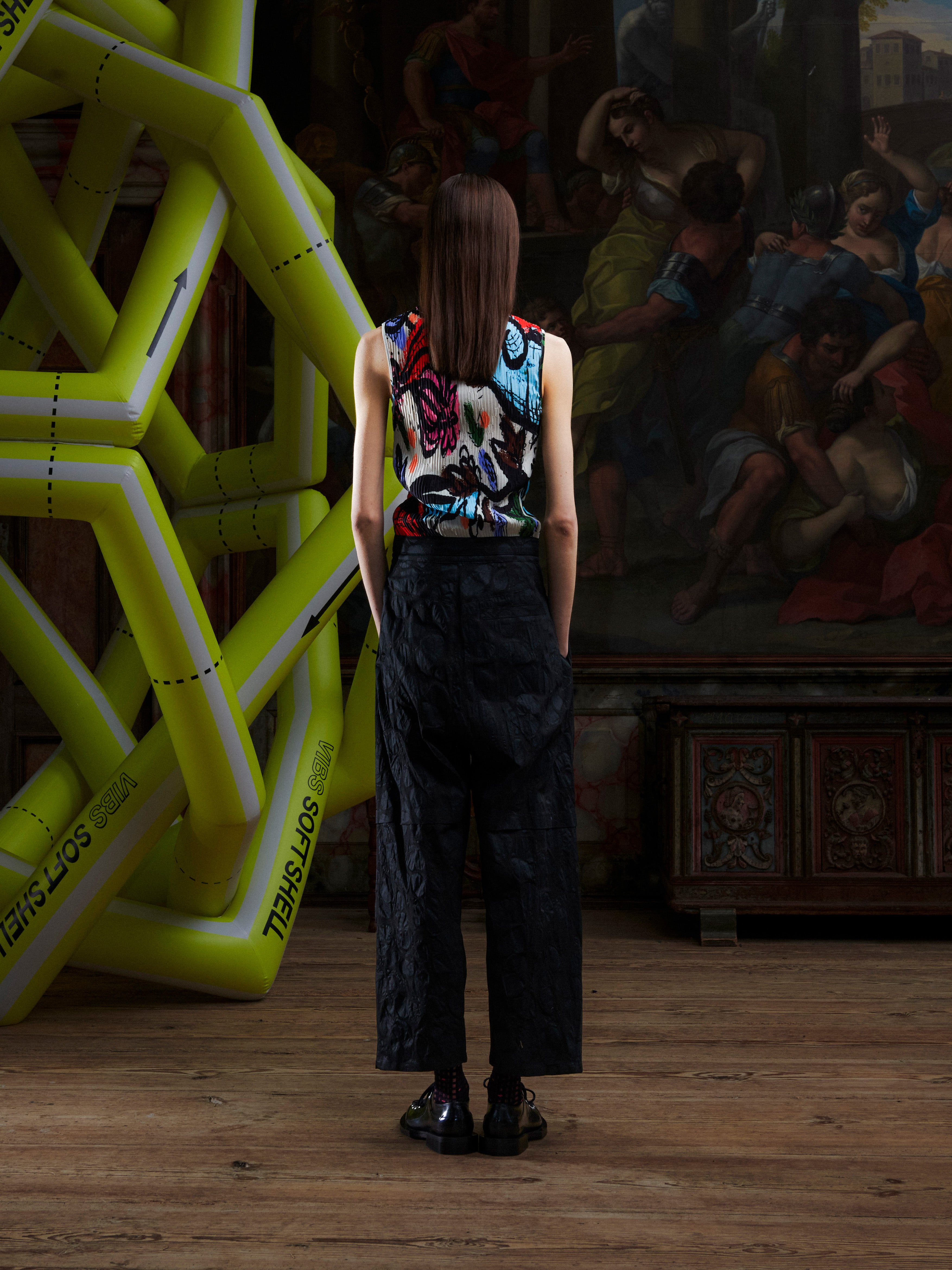 Back view of woman in a colorful top and black pants standing in front of an artistic backdrop with a large inflatable sculpture.