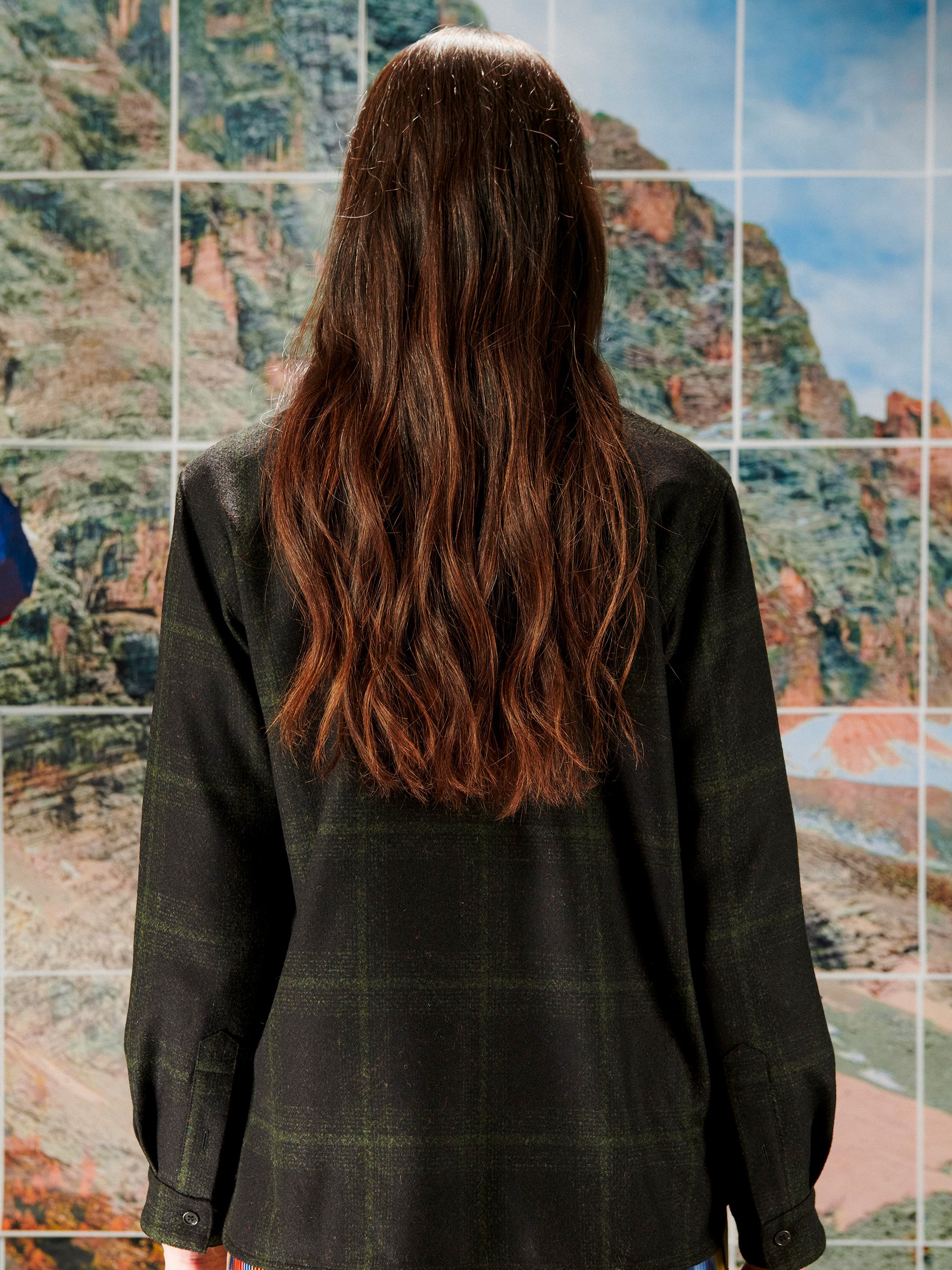 Woman wearing a black plaid shirt in front of a colorful abstract wall.