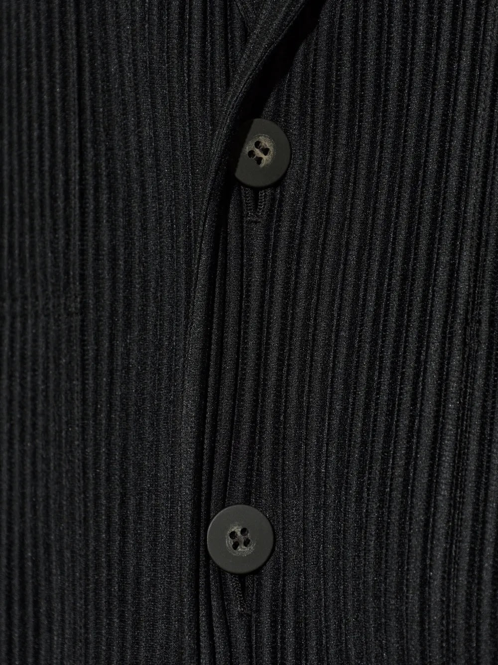 Homme Plissé Issey Miyake April SS26 Basic Jacket, close-up of the pleated black fabric showing fine vertical pleat texture and matte four-hole button detail at the front closure